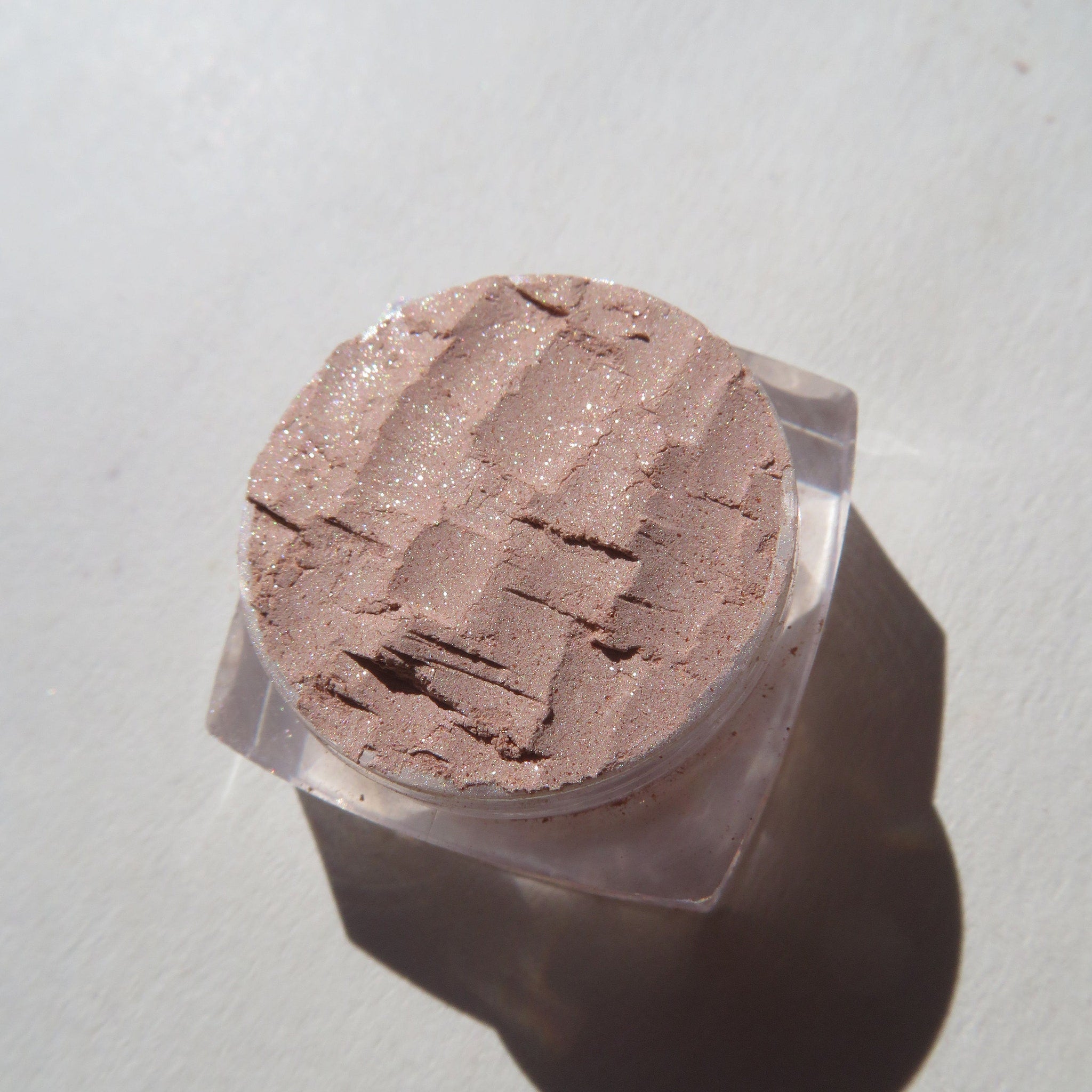 Side view of loose mineral eyeshadow in frosty golden champagne with shimmer particles catching light