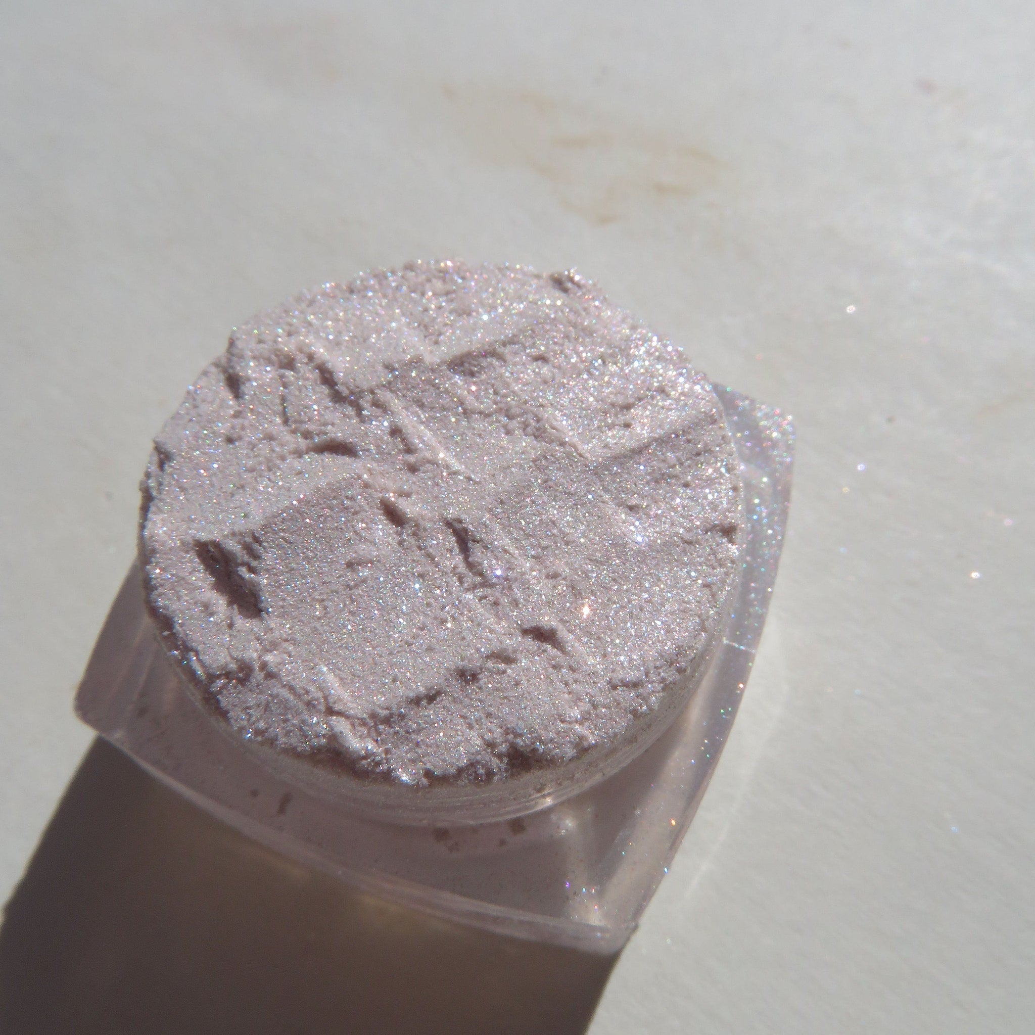 Hand applying sheer pink sparkly glitter eyeshadow to eyelid with fingertip, showcasing shimmer effect