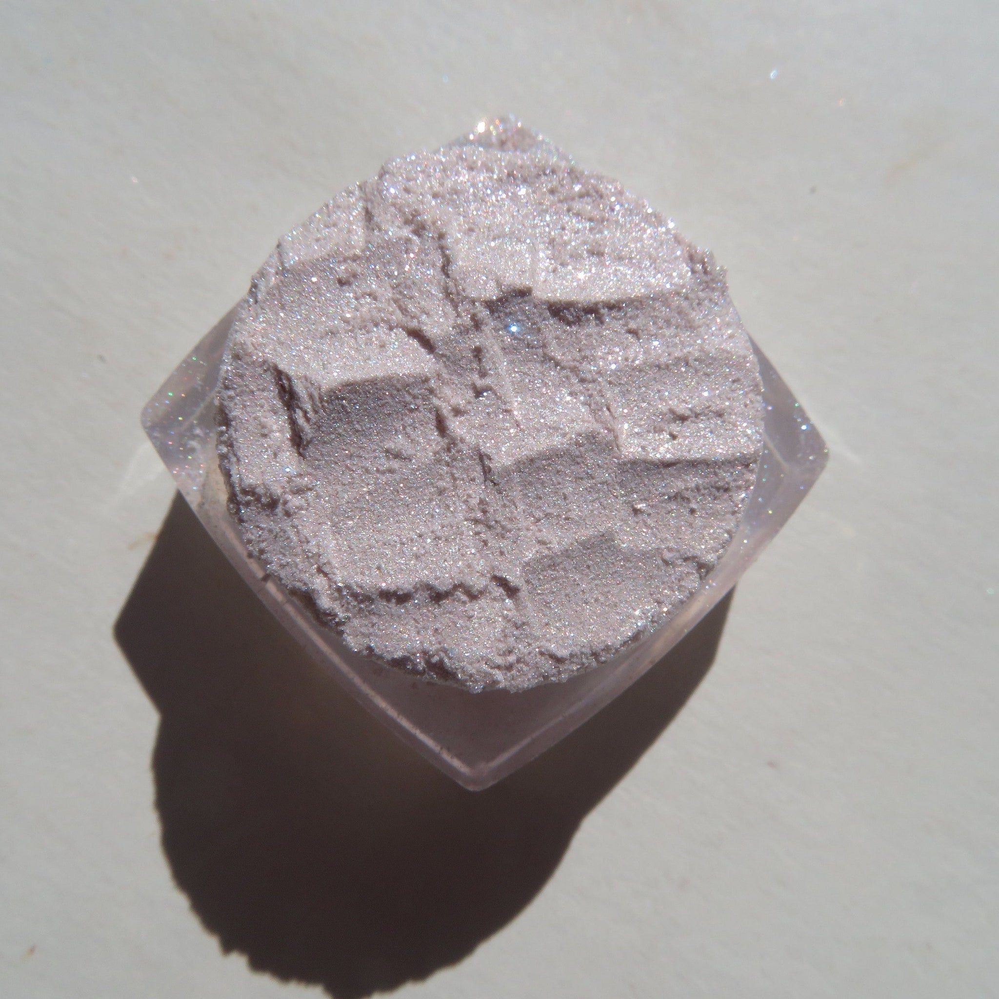 Side view of sheer pink sparkly glitter eye shadow pot showing shimmering mineral texture and vegan label