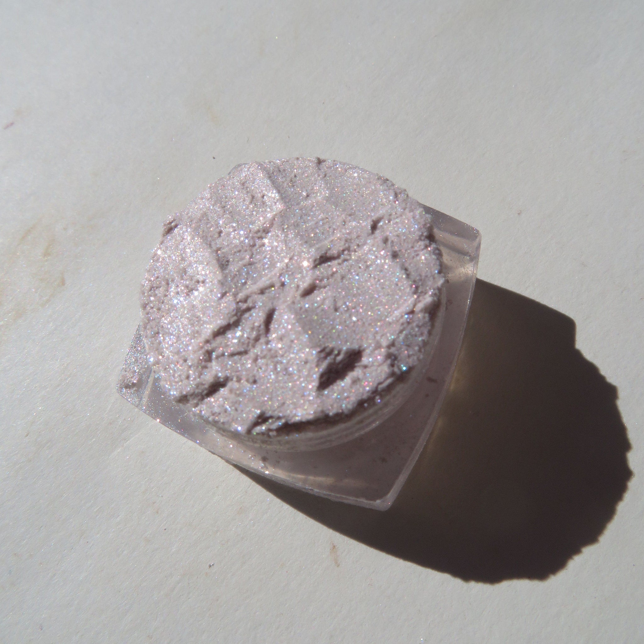 Pink glitter eyeshadow compact with sleek silver case and clear lid, showcasing shimmer texture