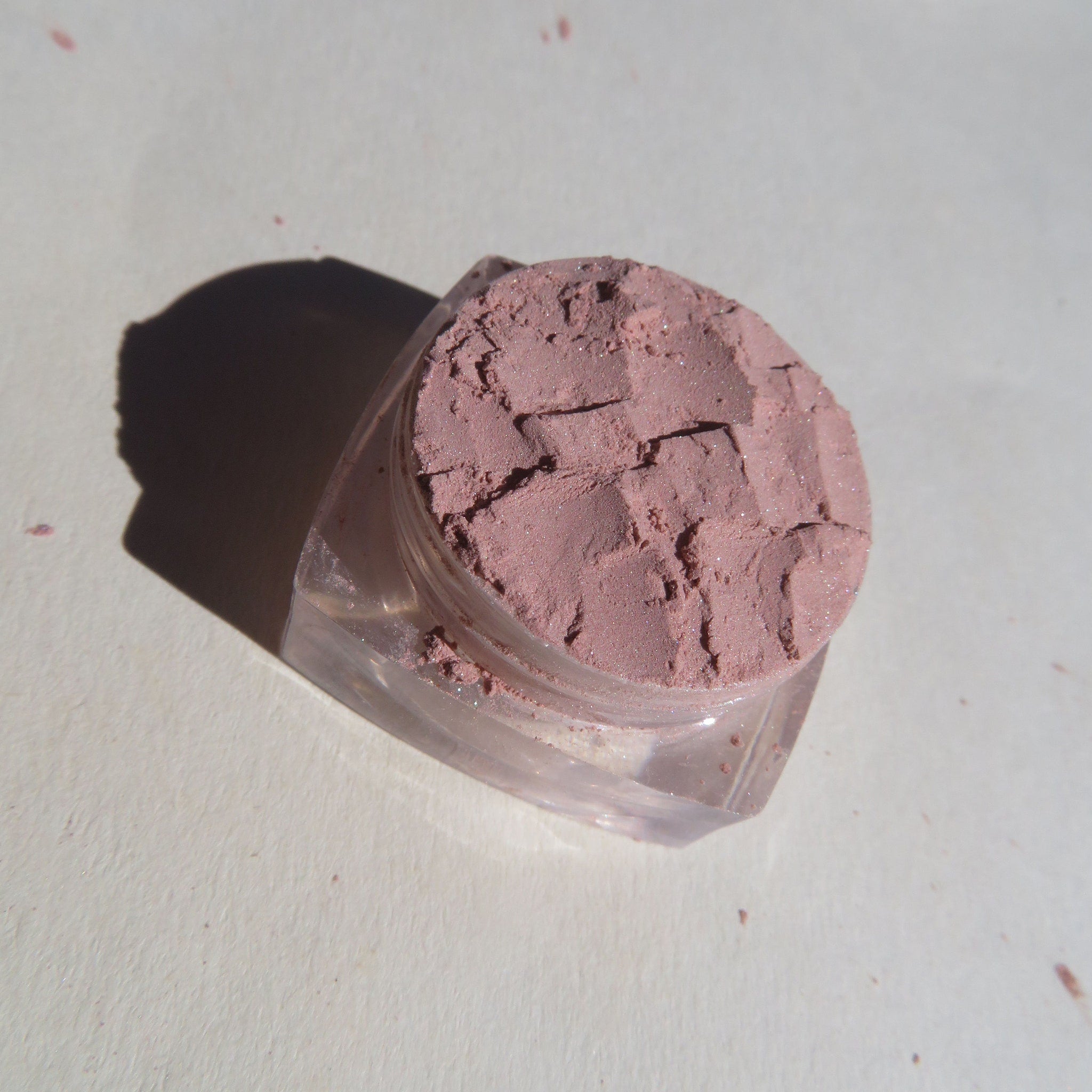 Side view of sandy brown shimmer loose mineral eyeshadow in a clear jar with gold lid, showcasing fine pigment texture.