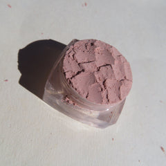 Side view of sandy brown shimmer loose mineral eyeshadow in a clear jar with gold lid, showcasing fine pigment texture.