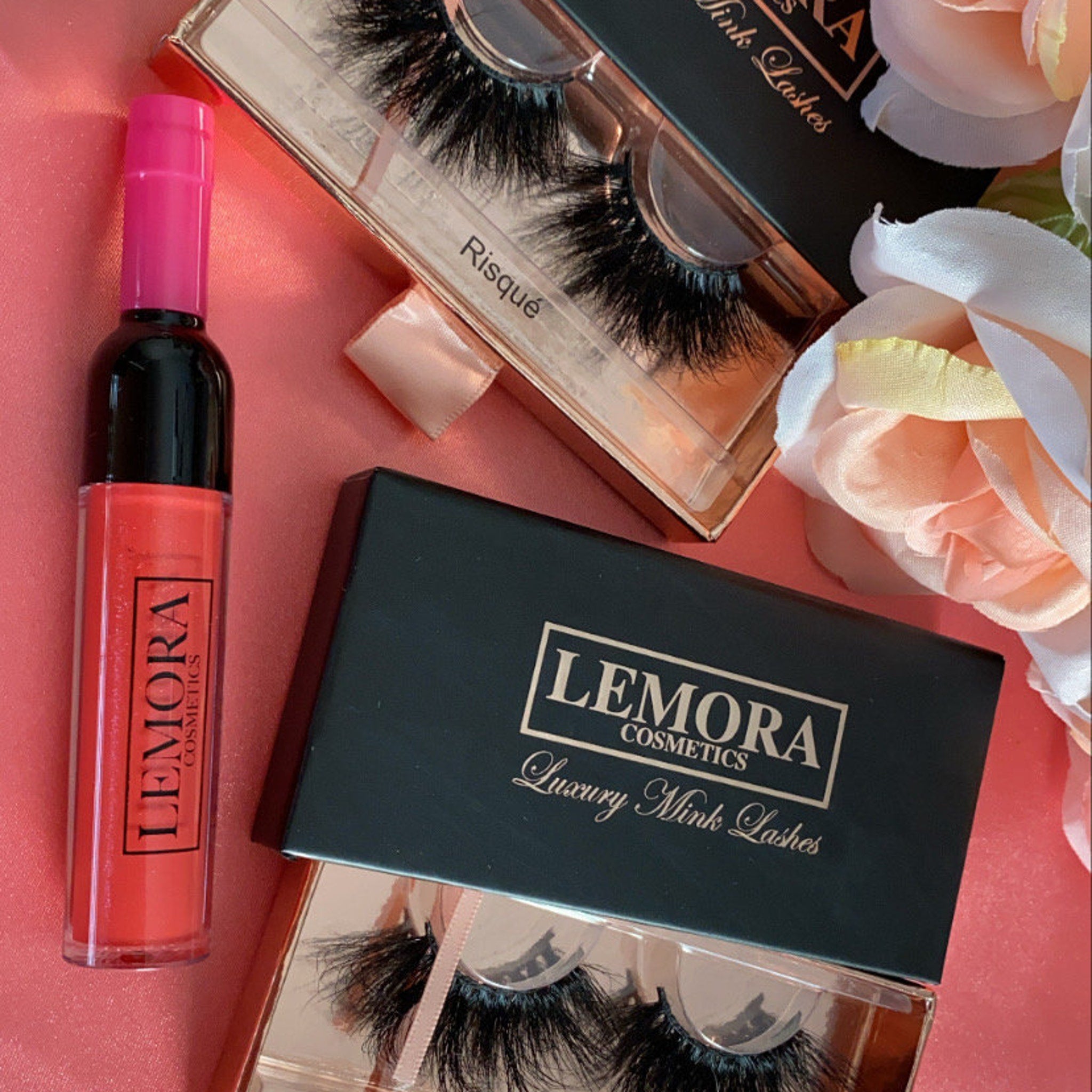 False eyelashes with black mink, clear packaging, and LEMORA Cosmetics branding on packaging and lip gloss bottle