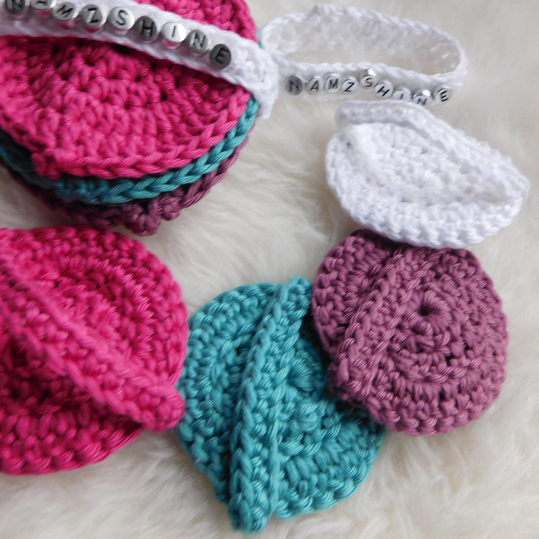 Crochet coasters in pink, teal, white, and purple colors, with beaded text detail