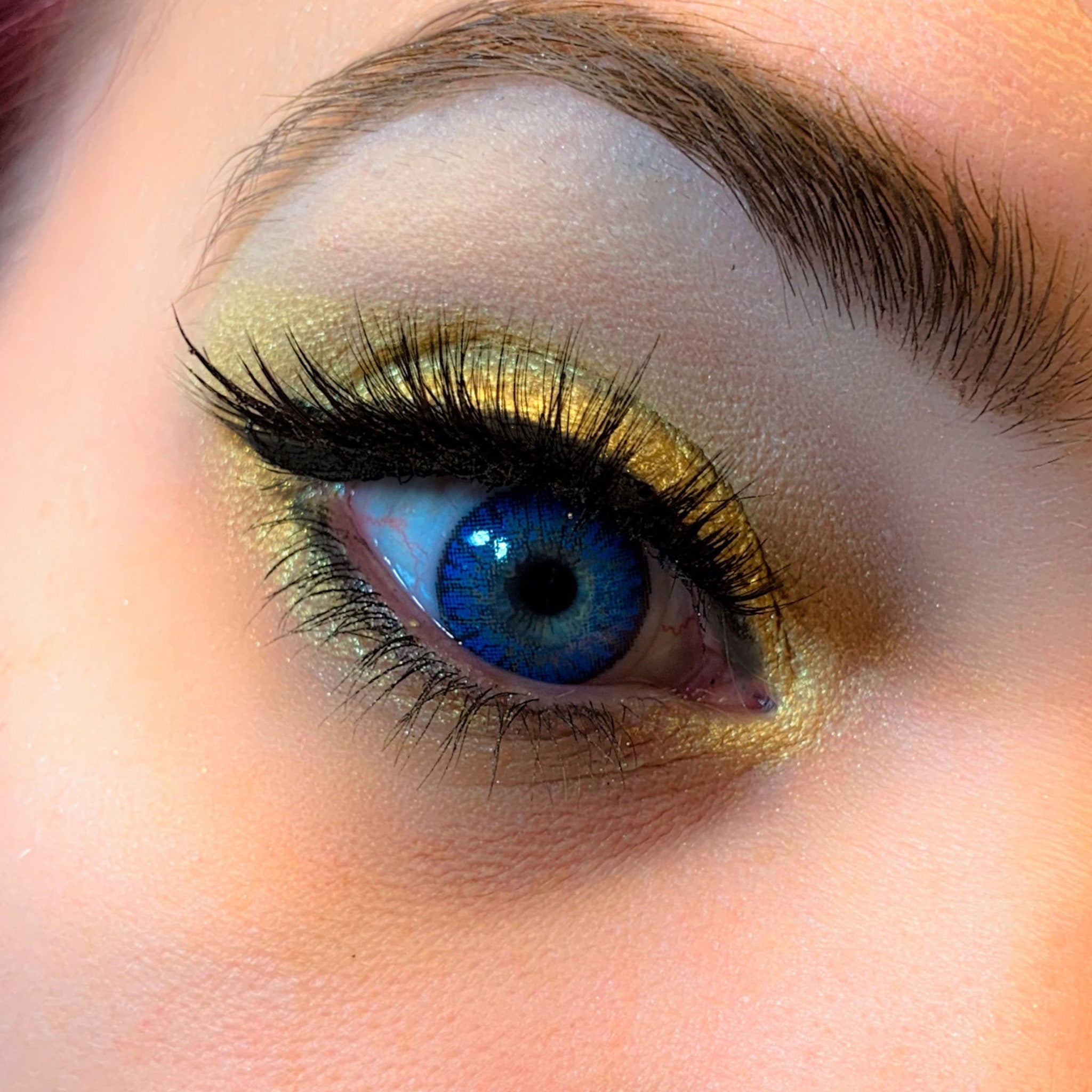 Blue eye contact lens with gold eyeshadow and black eyelashes, close-up view