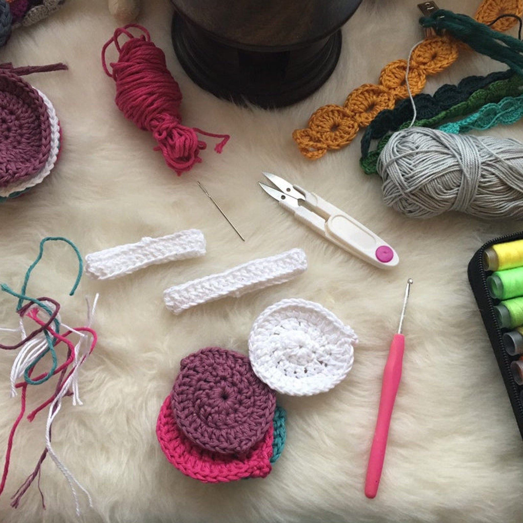 Crochet supplies: pink, white, and gray yarn with crochet hooks and scissors on a fluffy surface