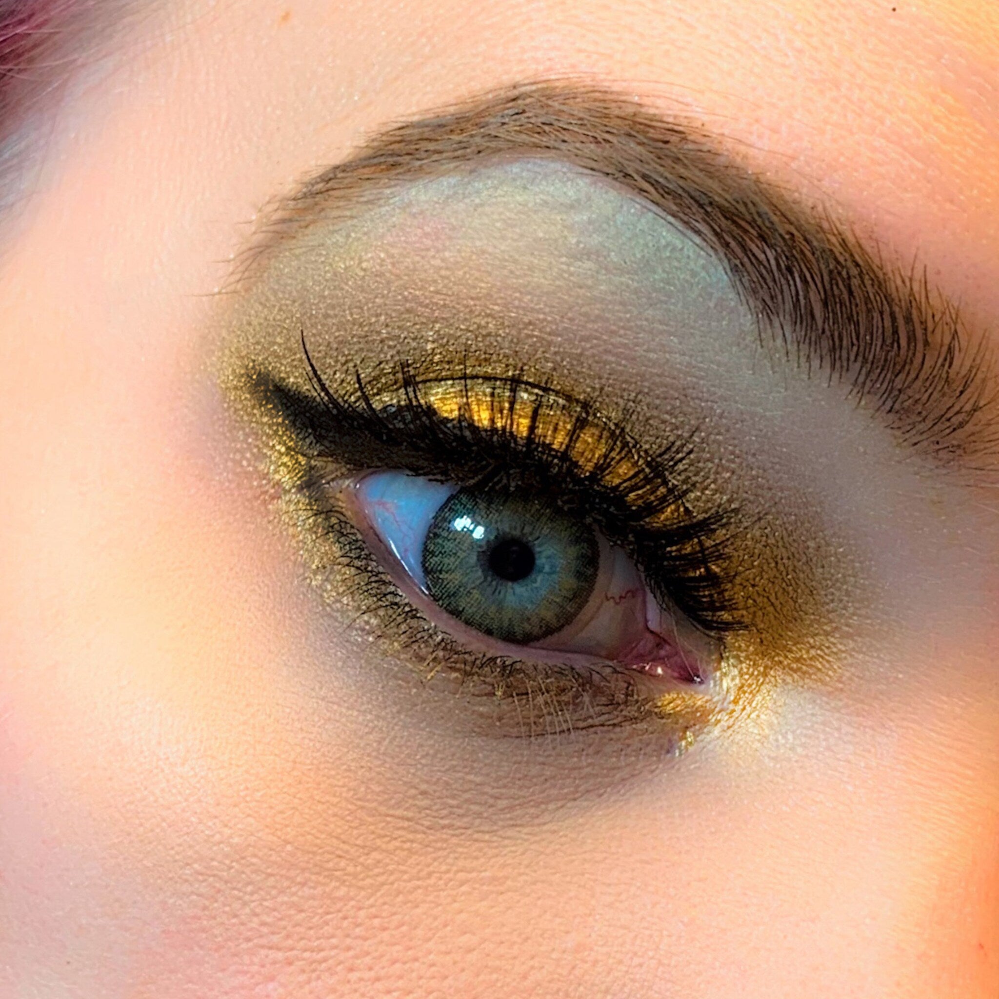 Side view of Halo Metallic Eyeshadow pot showcasing shimmering bronze pigment and sleek compact design