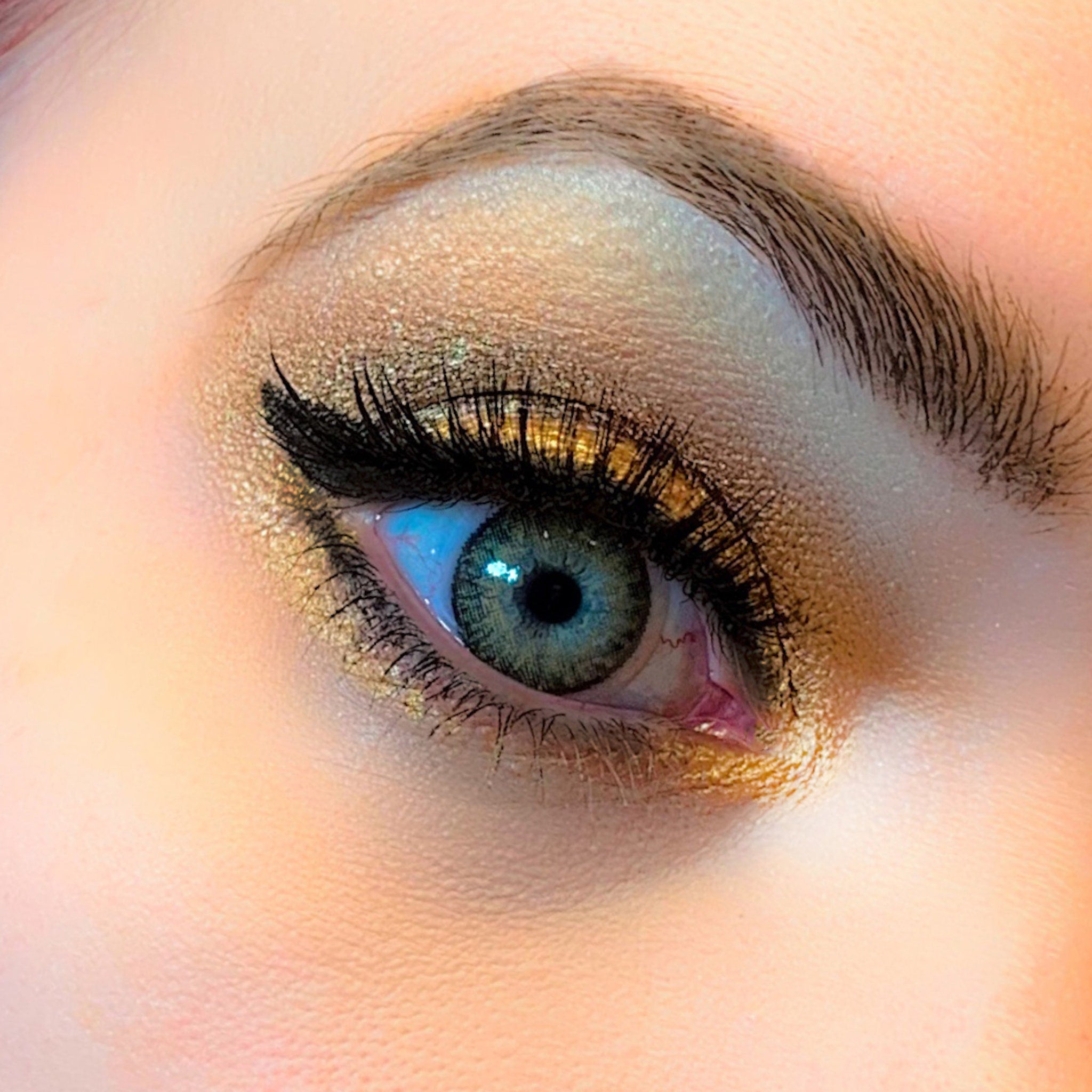 Eye makeup with gold eyeshadow, black eyeliner, and blue-green eye color, close-up view