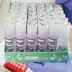Lip oil bottles with white caps, black labels, and Beauty Treats branding in display box