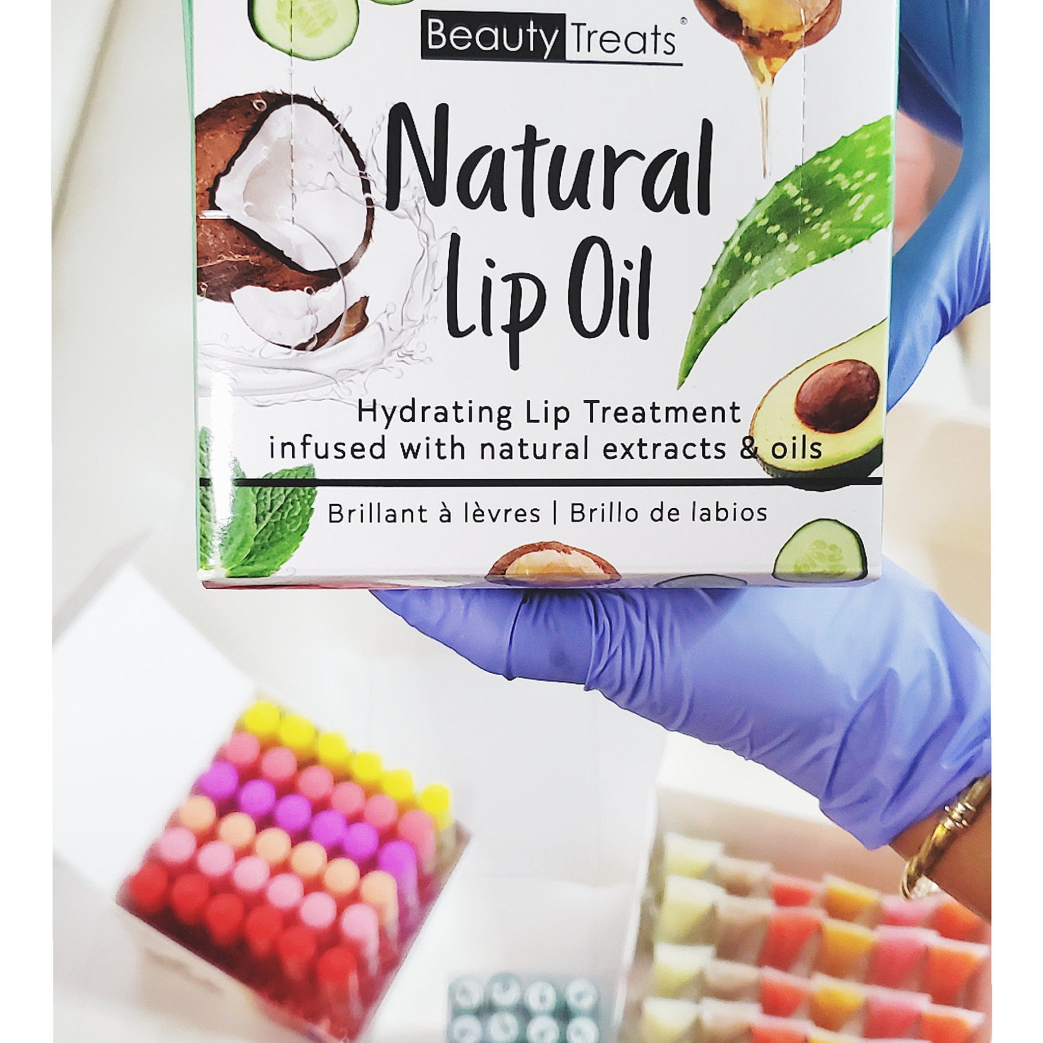 Lip oil box with white background, Beauty Treats branding, and natural ingredient illustrations being held by a gloved hand