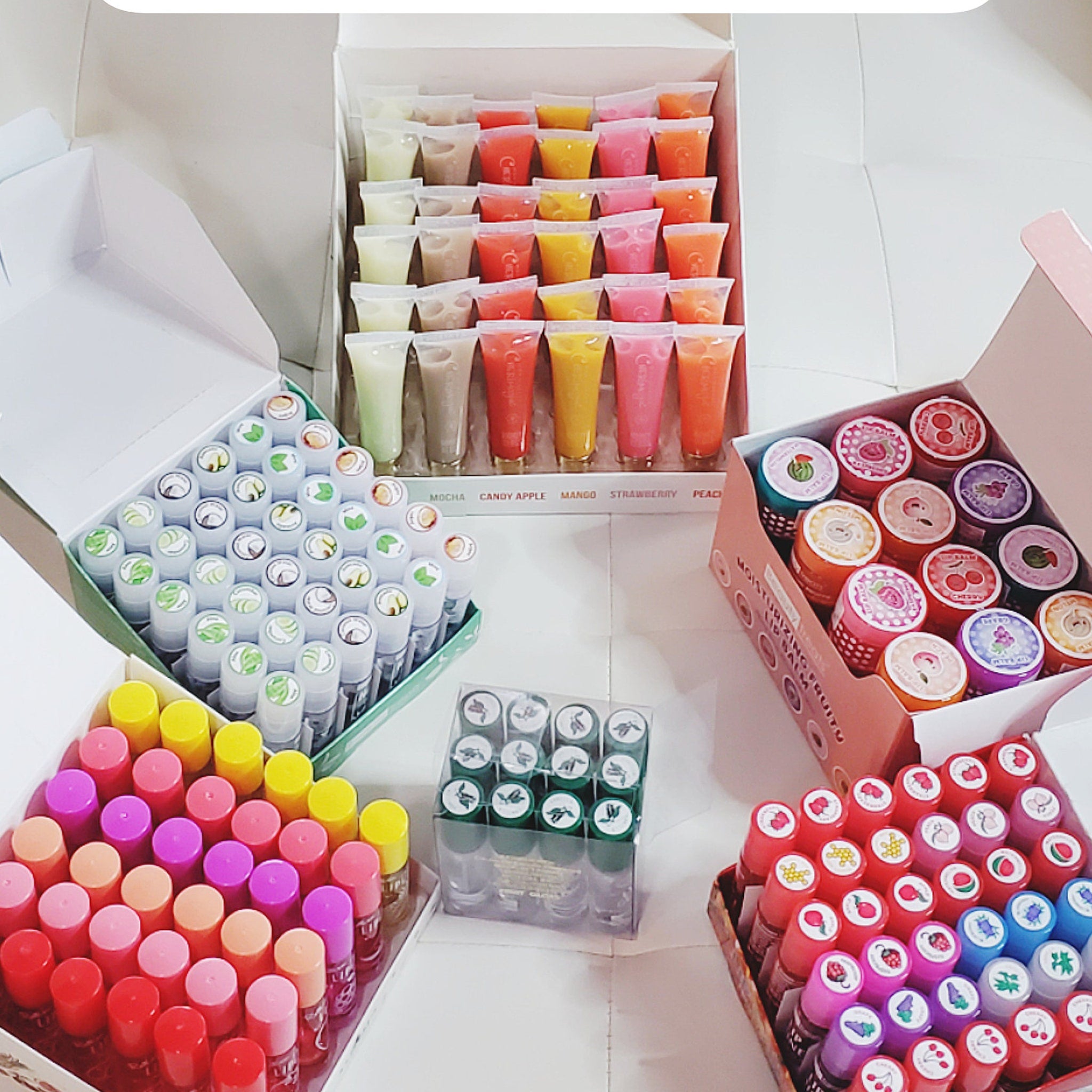 Lip gloss tubes in assorted colors, clear tubes with colorful contents, and boxes of lip balm
