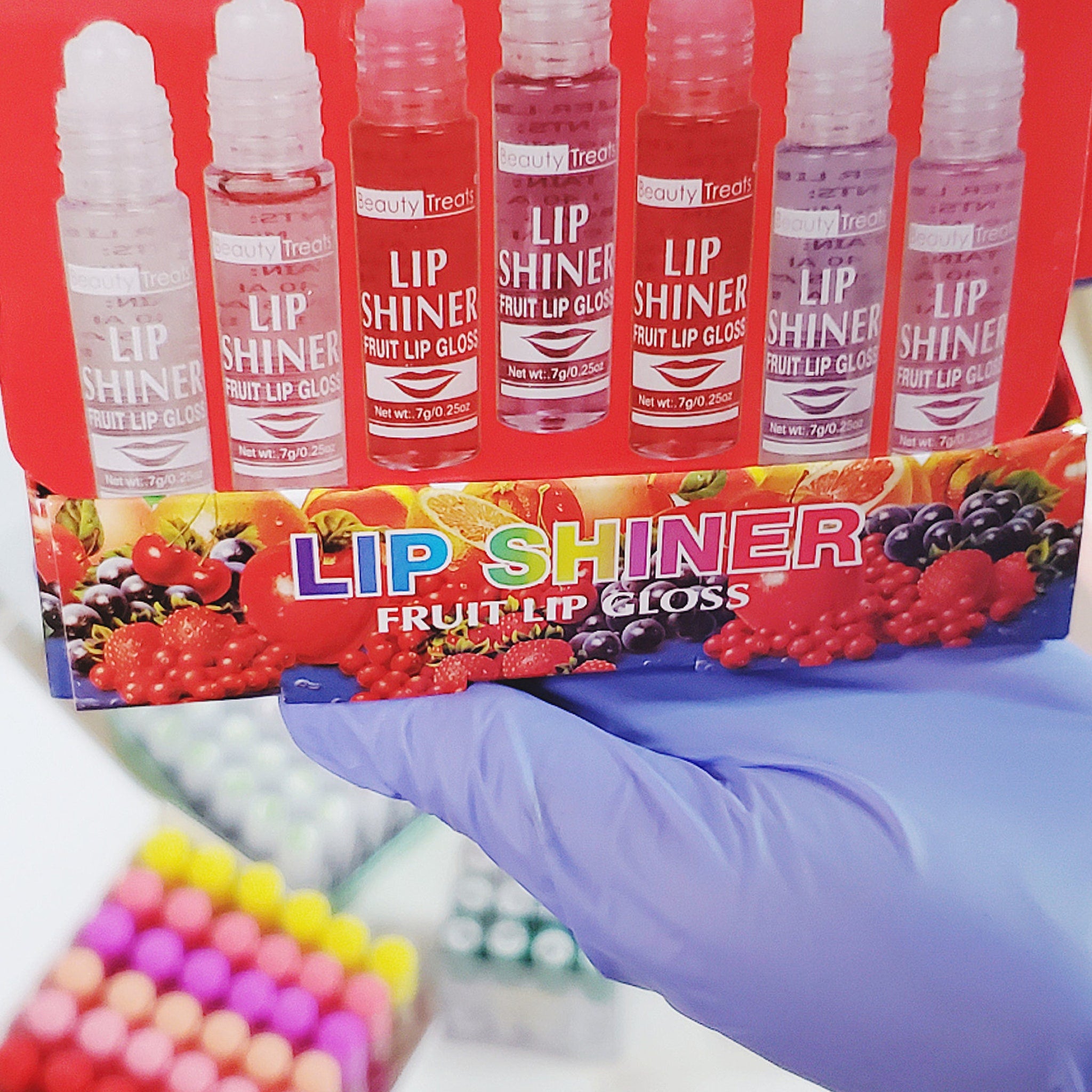 Lip gloss tubes with clear, pink, and purple liquid, Beauty Treats brand visible, held by gloved hand