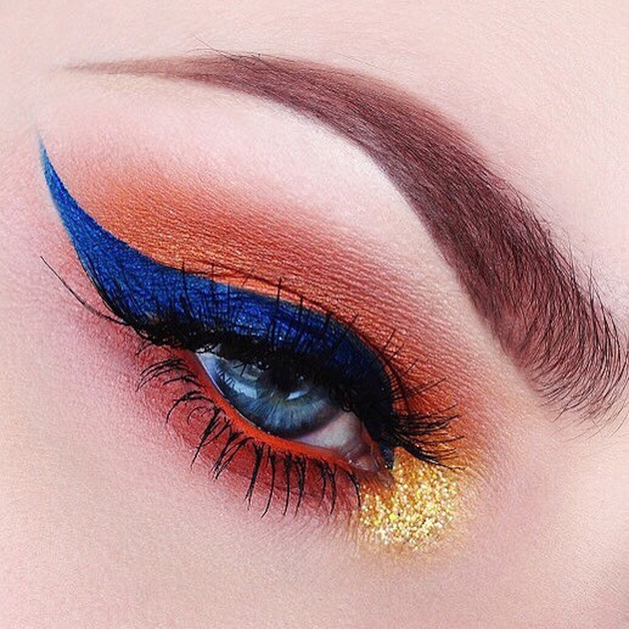 Eye makeup with blue eyeliner, orange eyeshadow, and gold glitter application
