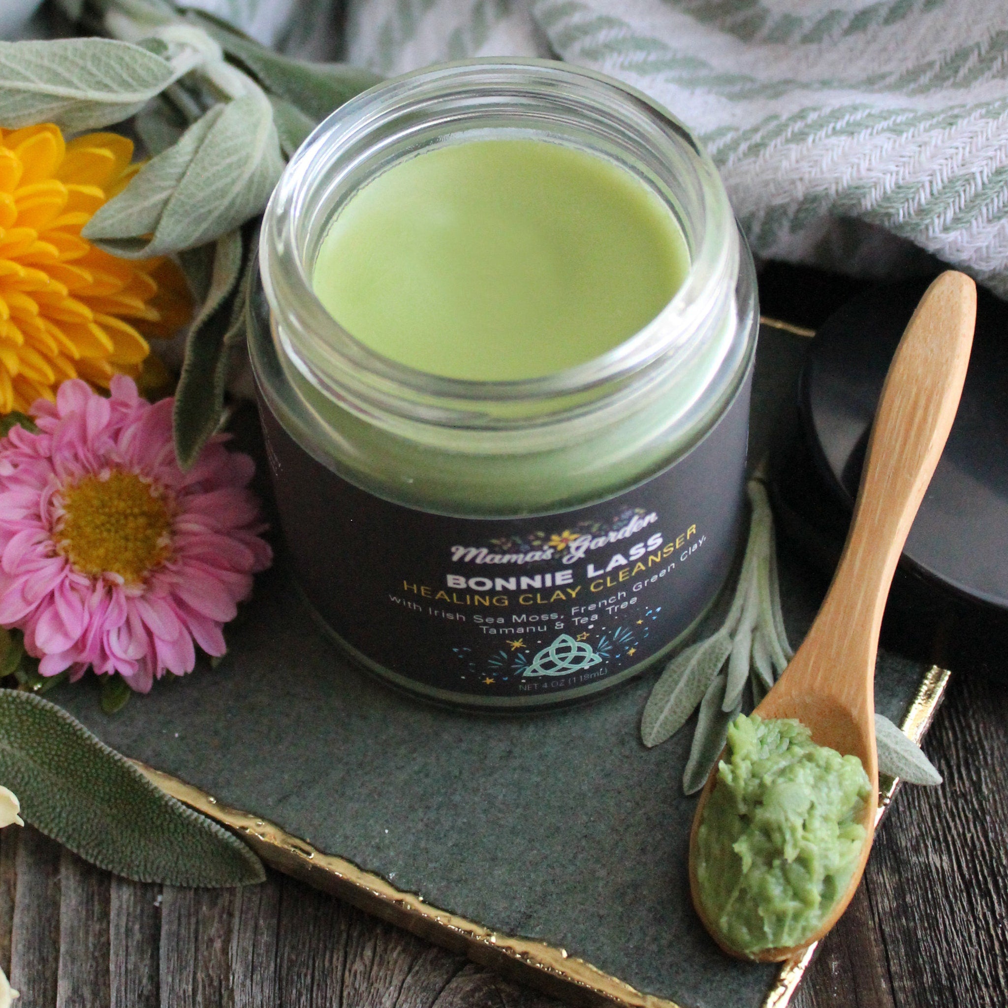 Clay cleanser jar with green paste, wooden spoon, and Mama's Garden label on black background