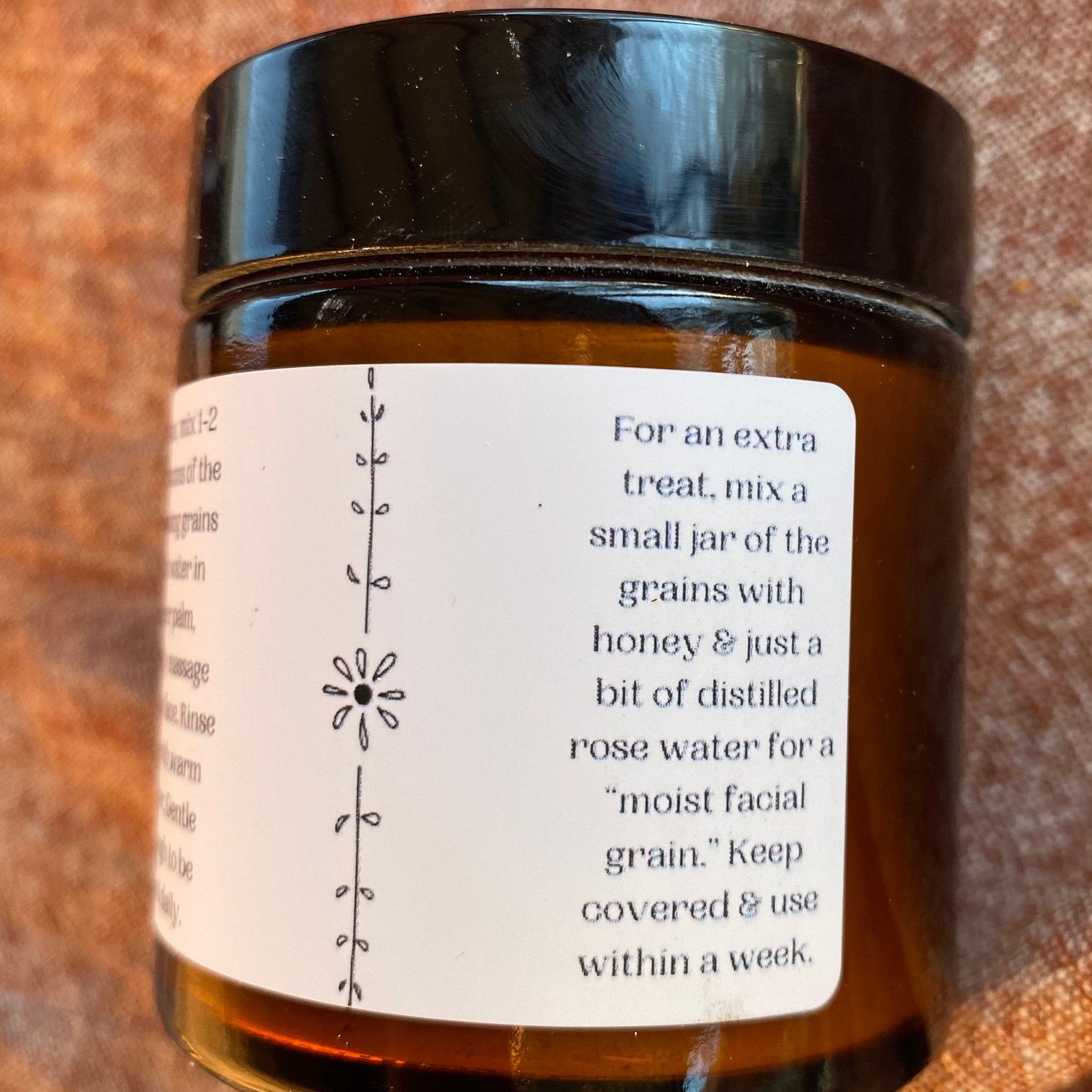 Brown glass jar with black lid and white label with text and floral design