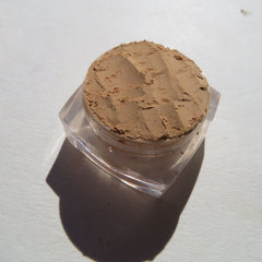 Powder makeup in tan color with textured surface in clear plastic jar