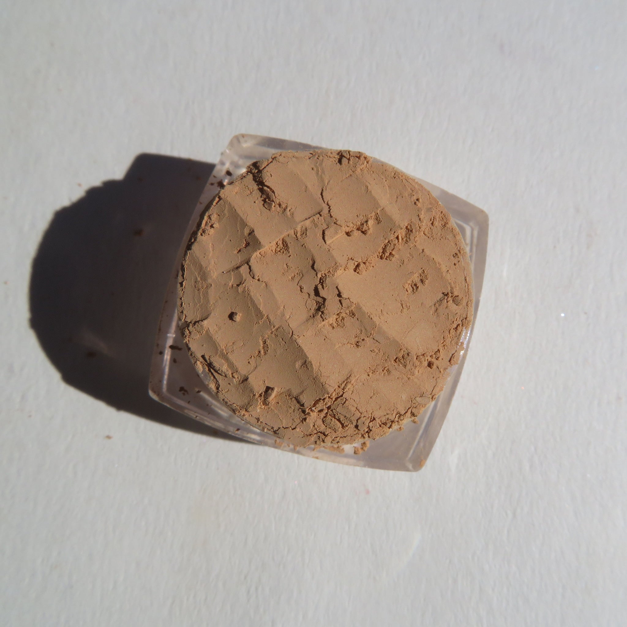 Powder makeup in beige color with textured surface inside a clear plastic container