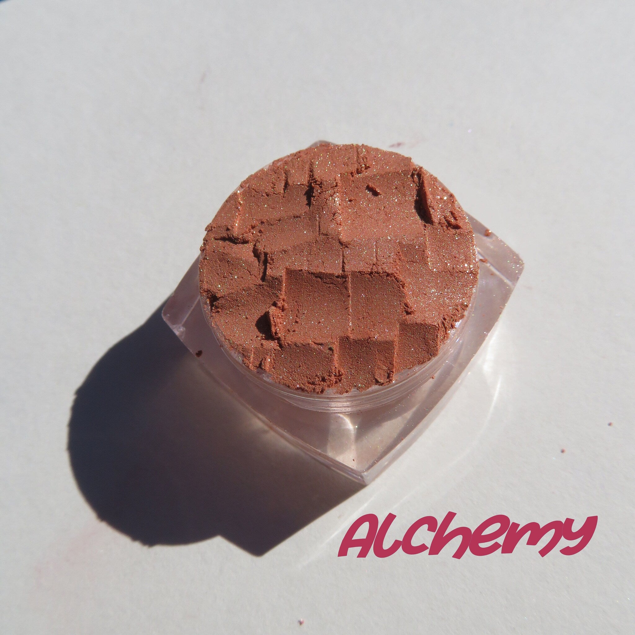 Side view of loose brown gold mineral eyeshadow with golden shimmer in a clear jar, showcasing texture and sparkle