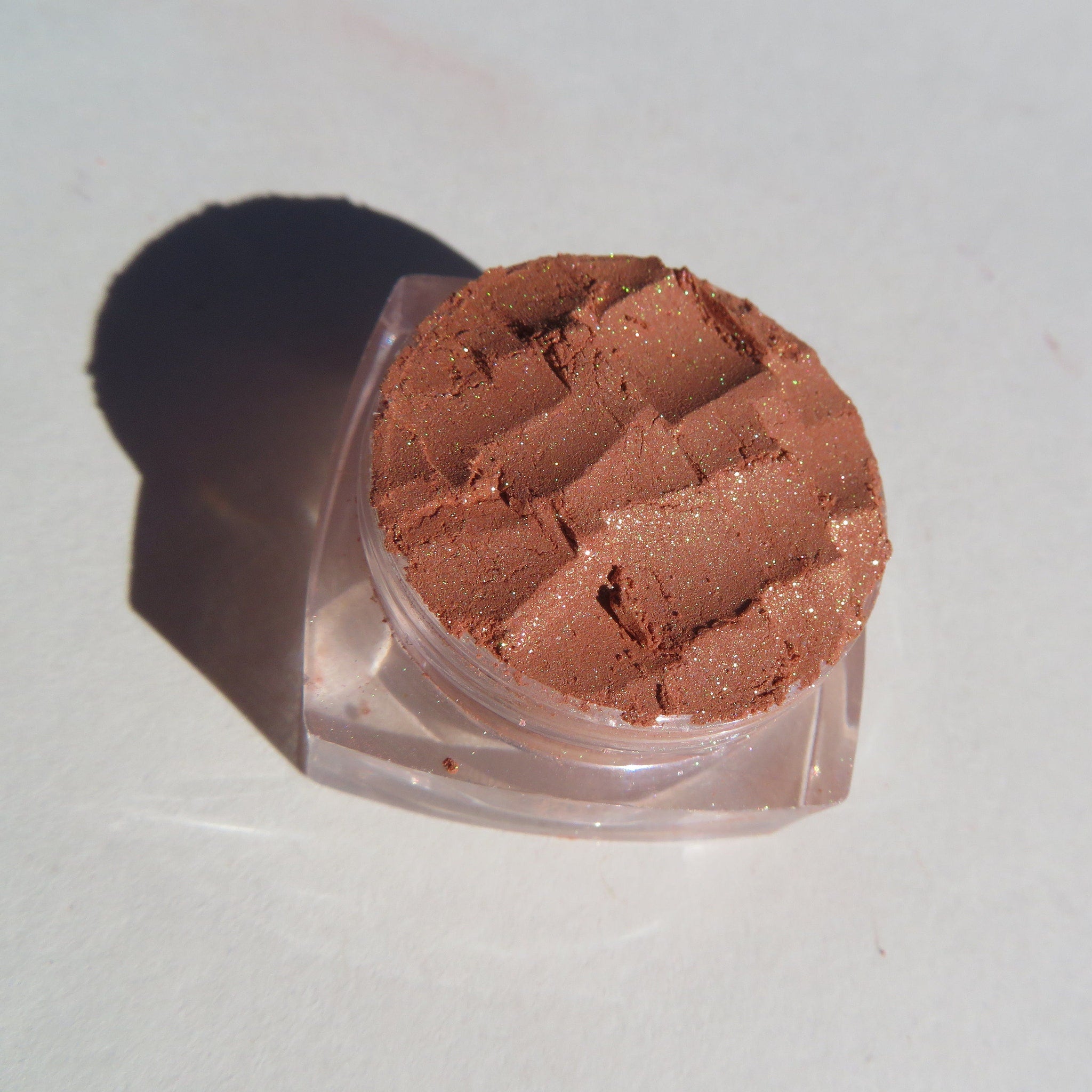 Side view of loose brown gold mineral eyeshadow with shimmer particles in a clear sifter jar