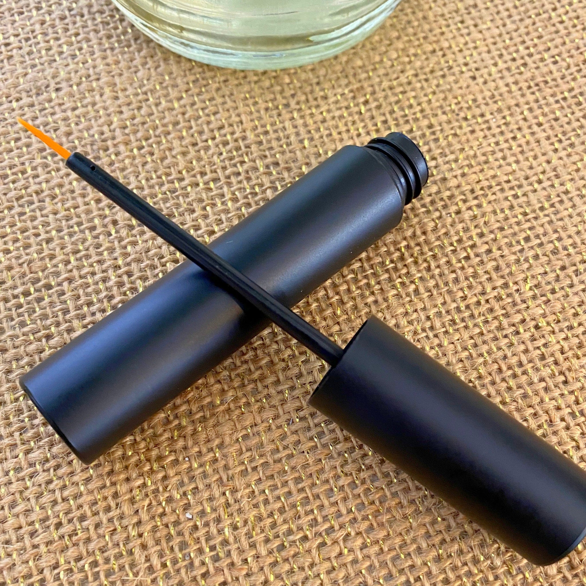 Black eyeliner applicator with orange tip on textured brown surface.