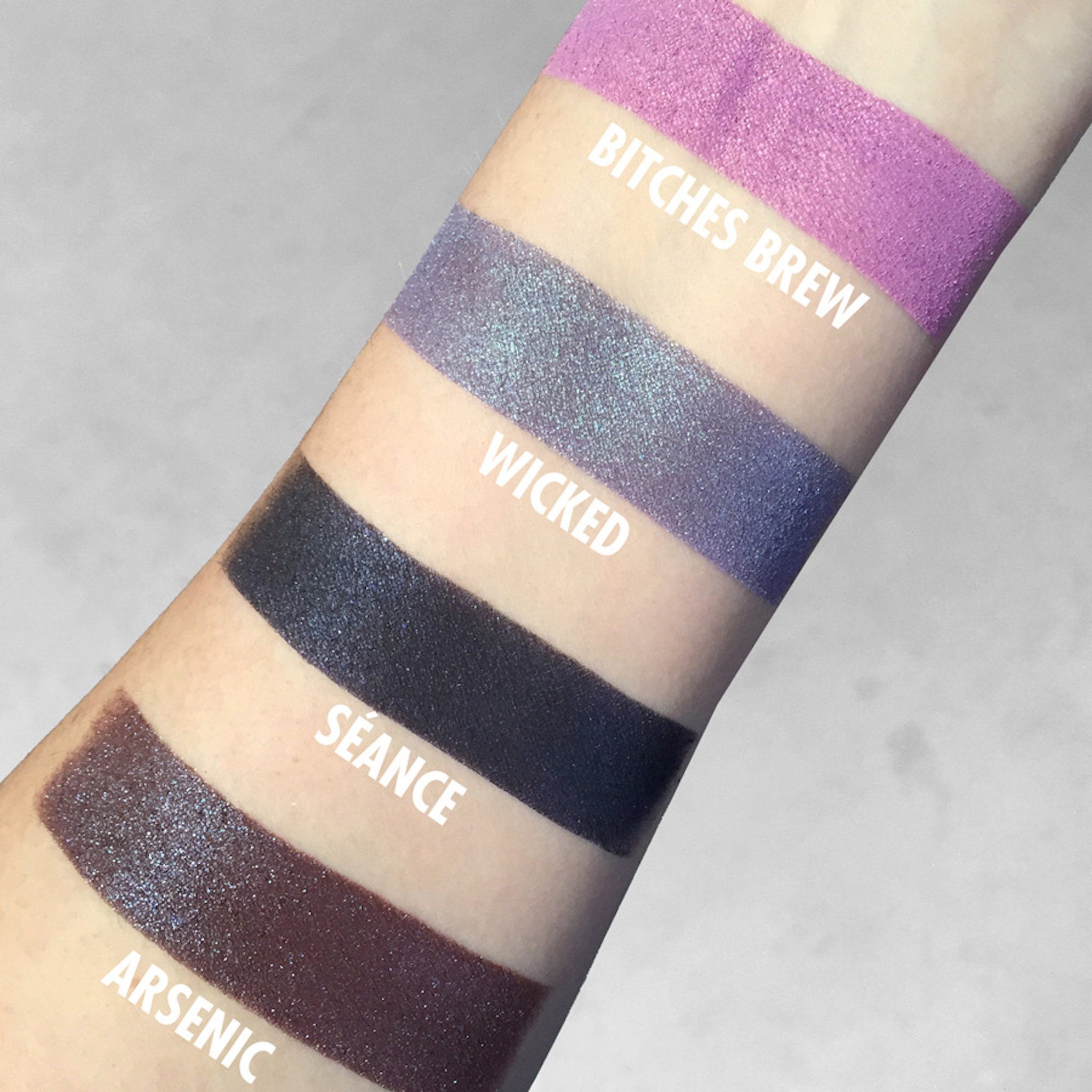 Eyeshadow swatches on arm in purple, blue, and black shades with glitter, text labels visible