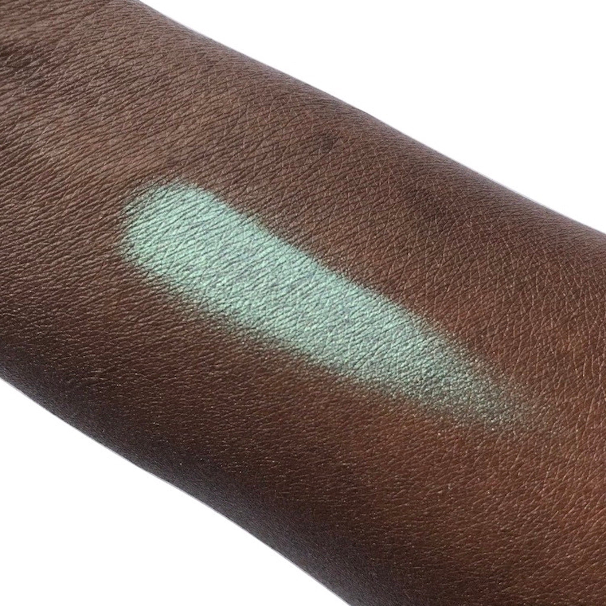 Eyeshadow swatch in mint green color on dark skin, showing texture and application