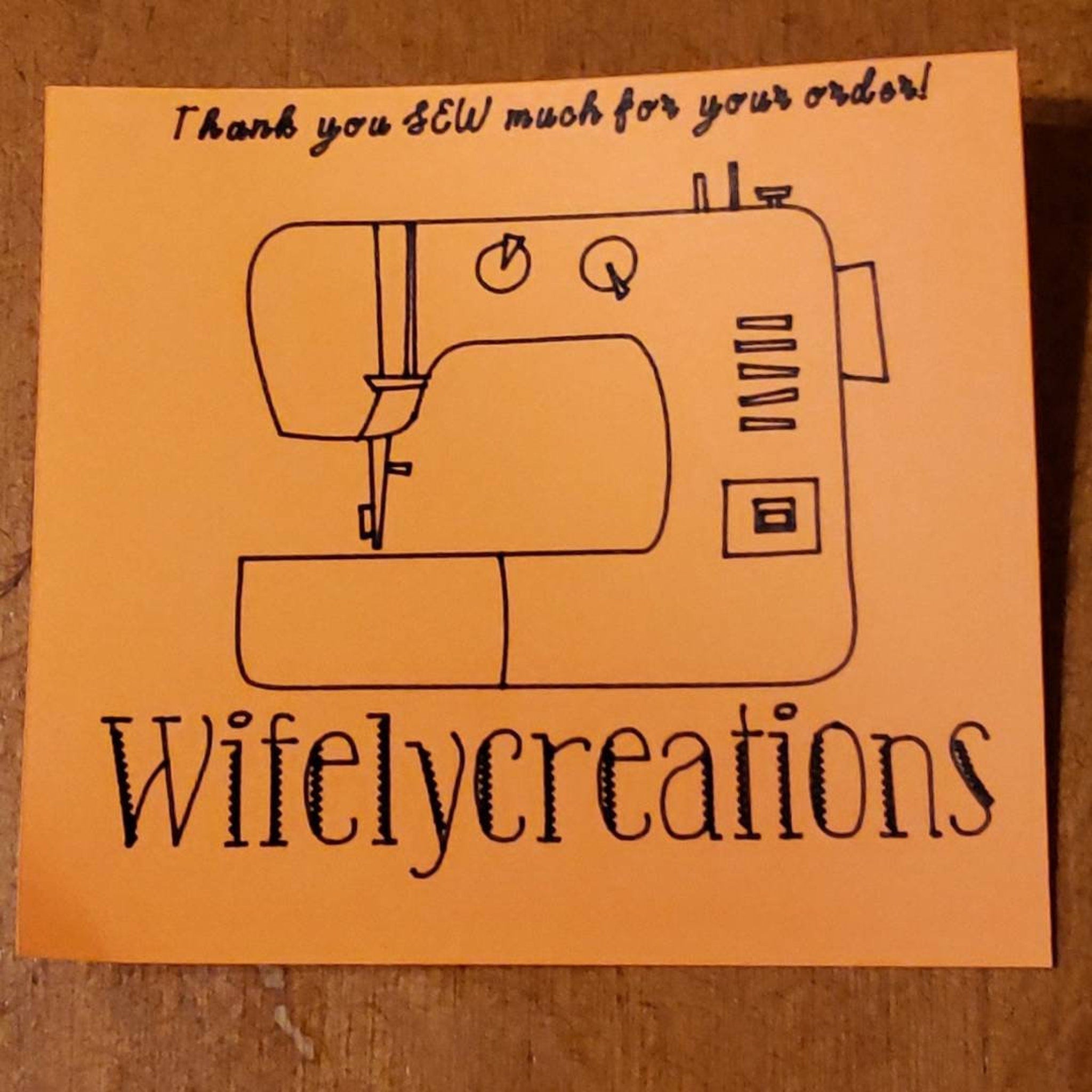 Orange paper with black sewing machine illustration and Wifelycreations text, thank you note
