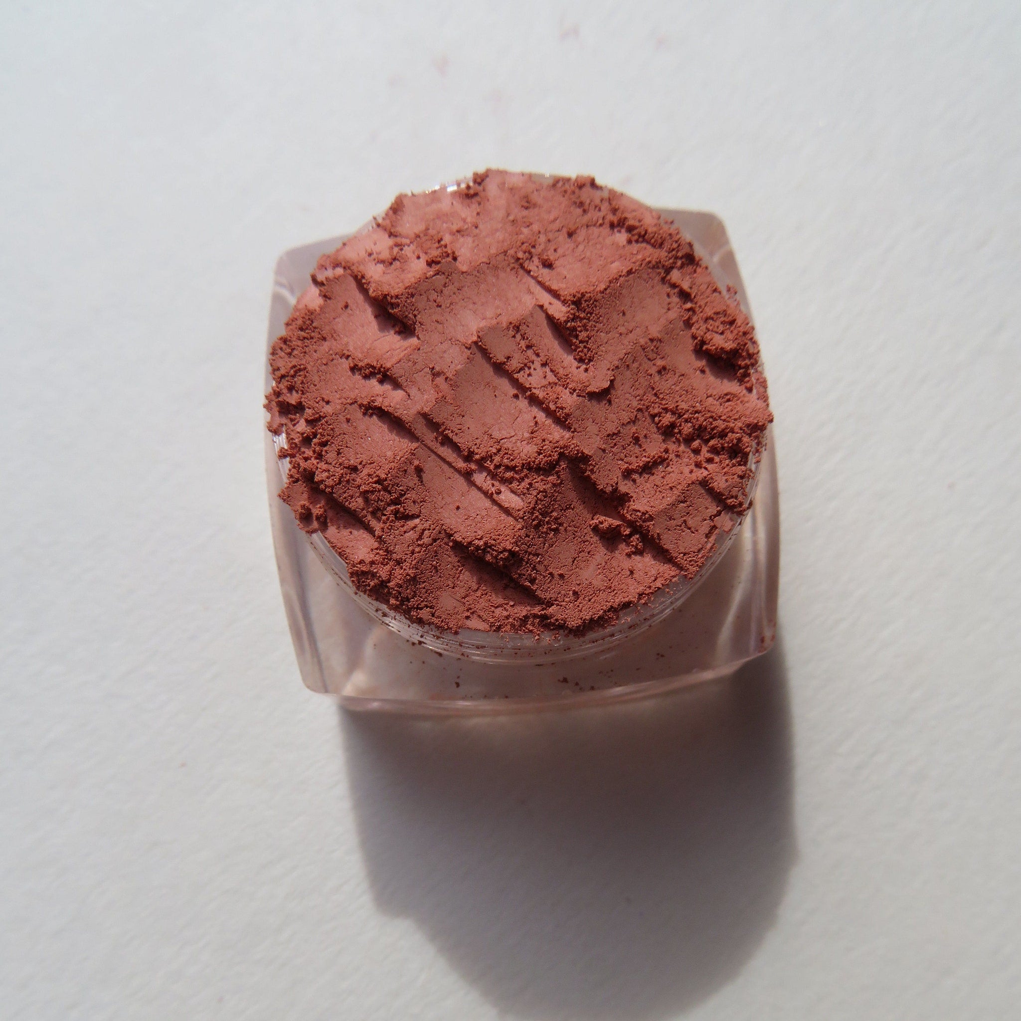 Close-up of burnt orange mineral eyeshadow powder spilling from jar, showcasing matte texture and vibrant pigment.