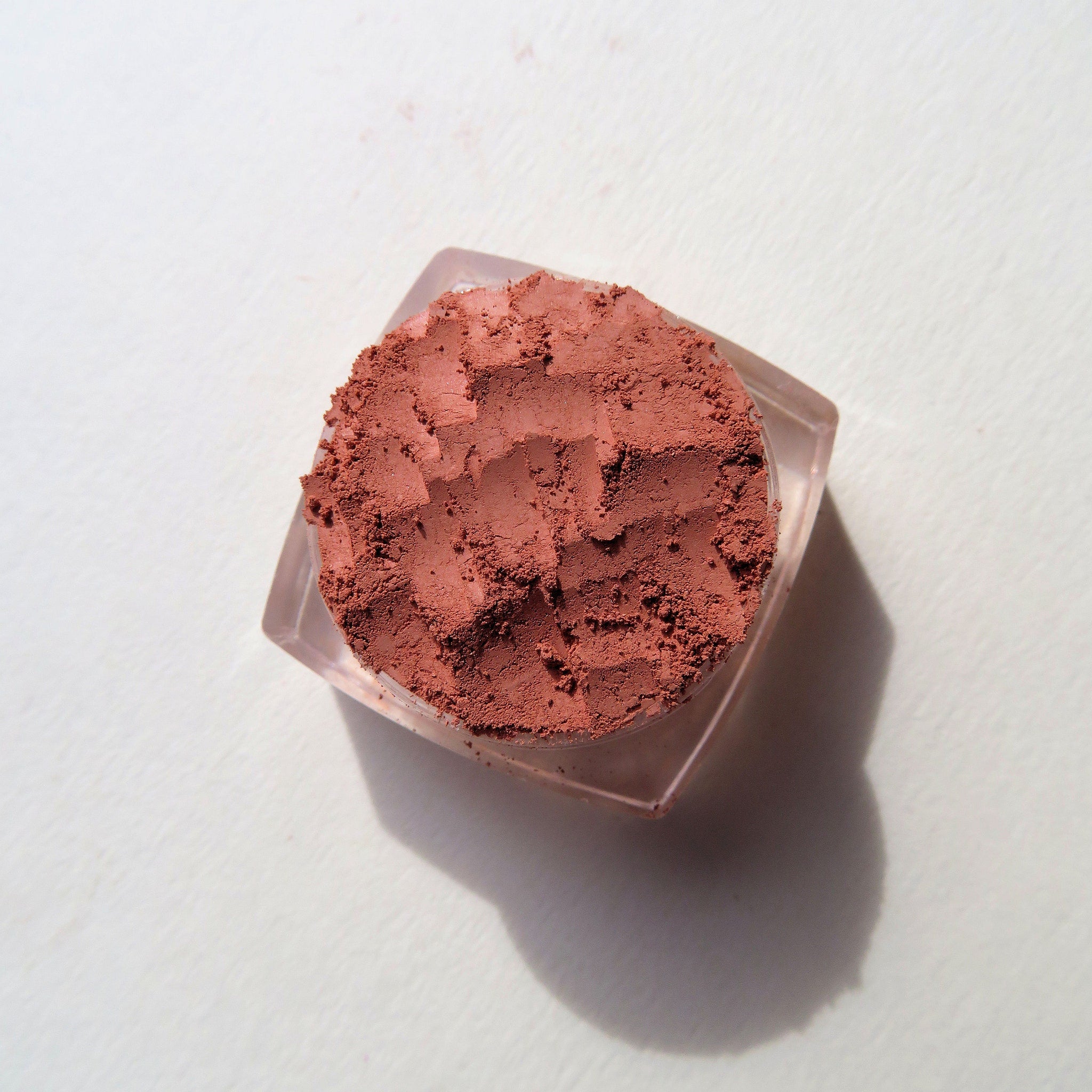 Side view of loose burnt orange mineral eyeshadow powder spilling from eco-friendly container onto surface