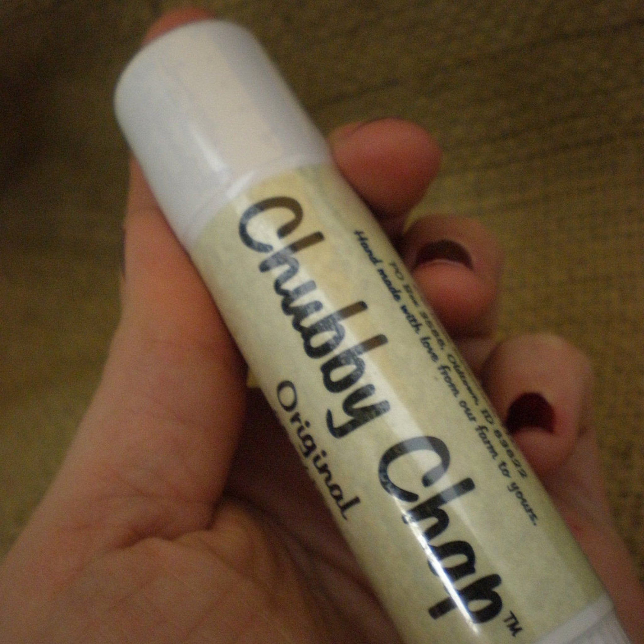 Lip balm stick with white cap and beige label, "Chubby Chap" text, held in hand