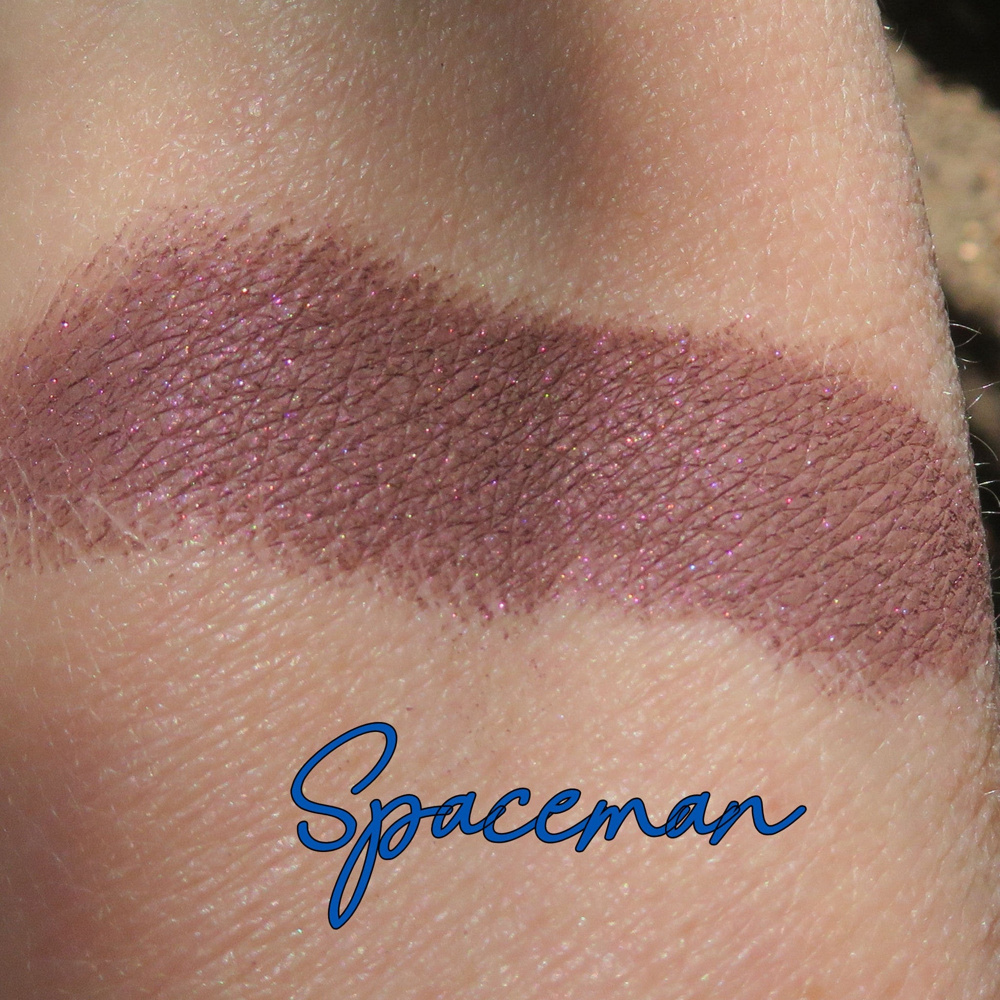Eyeshadow swatch in mauve with glitter, applied on skin, "Spaceman" text visible
