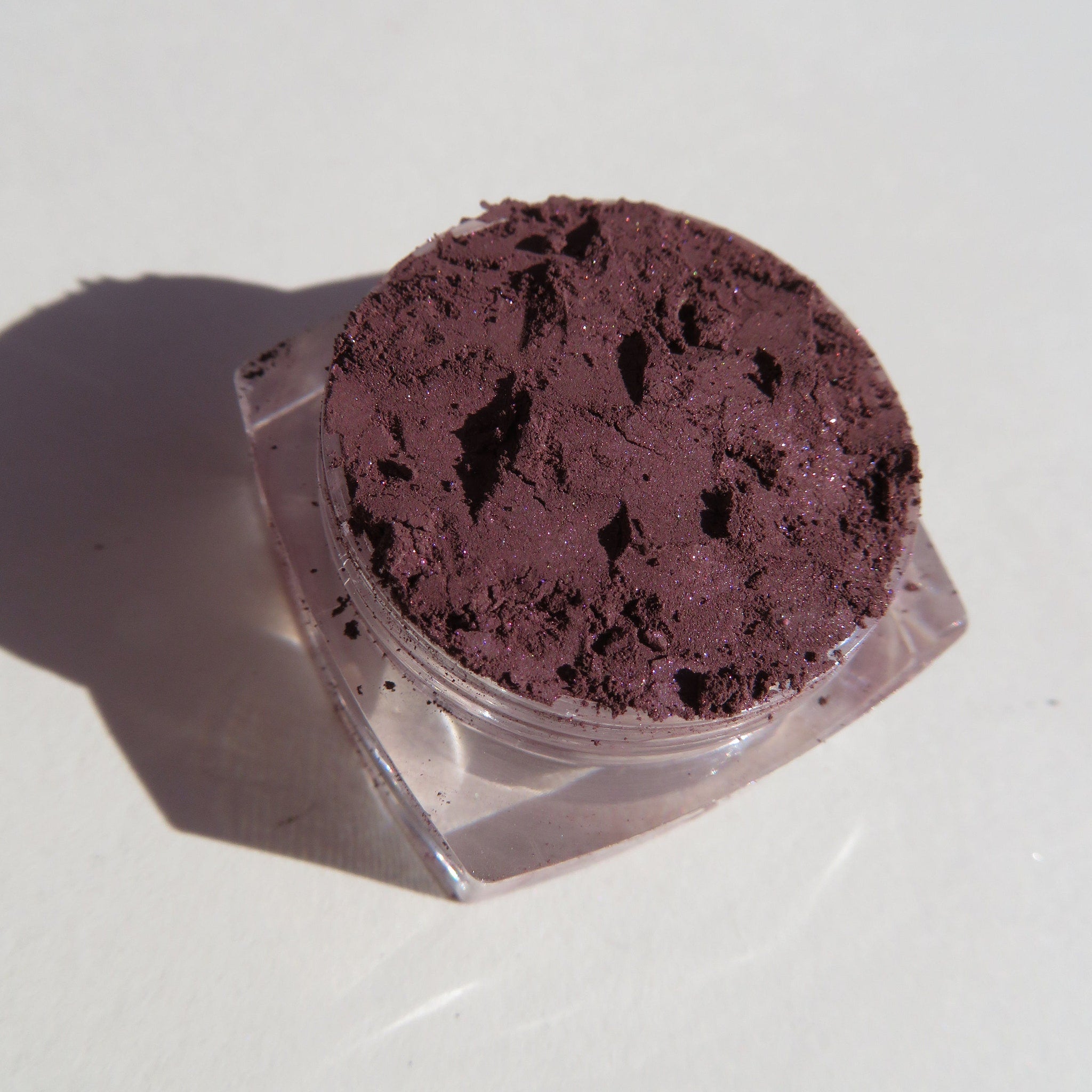 Powder eyeshadow in dark purple with glitter, in a clear plastic container