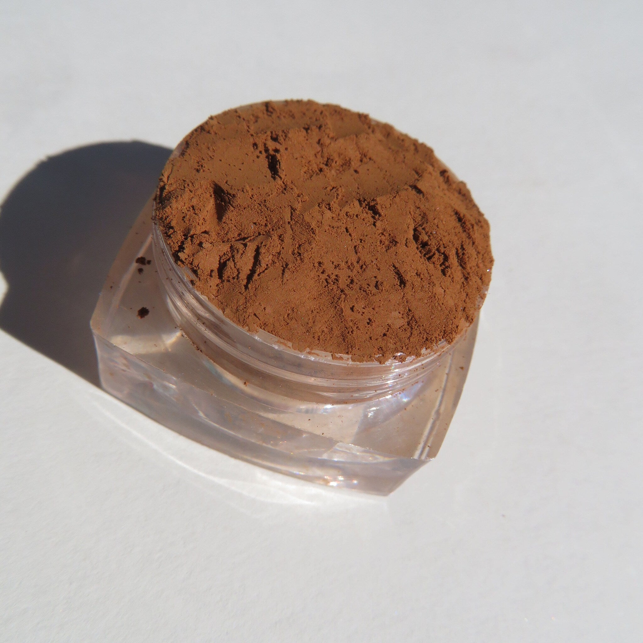 Close-up of sandy brown loose mineral eyeshadow with matte finish in a small jar