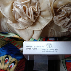 Merle Norman Cozy Nudes eyeshadow box with beige fabric and floral pattern background