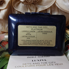 Makeup compact with navy blue case, gold label, and Merle Norman brand text visible