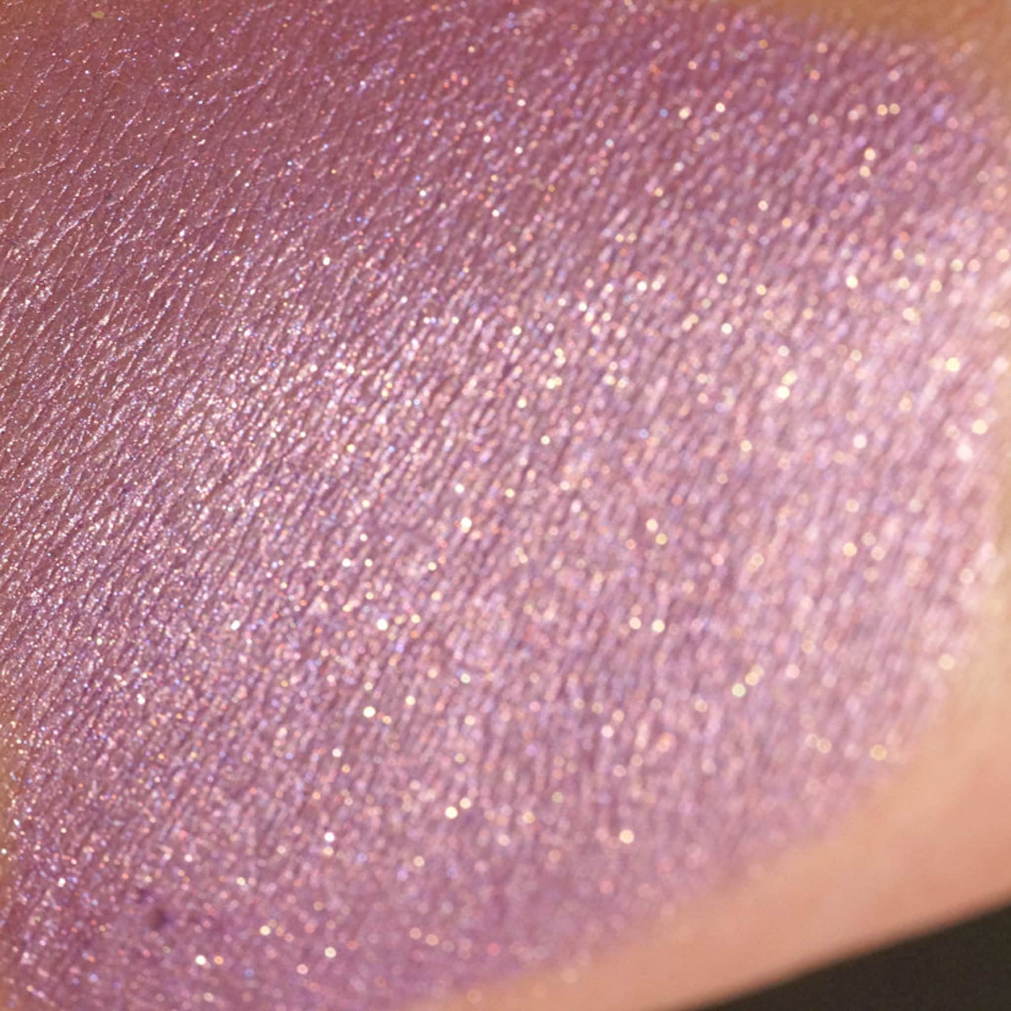 Eyeshadow swatch with pink shimmer, light texture, and skin tone background
