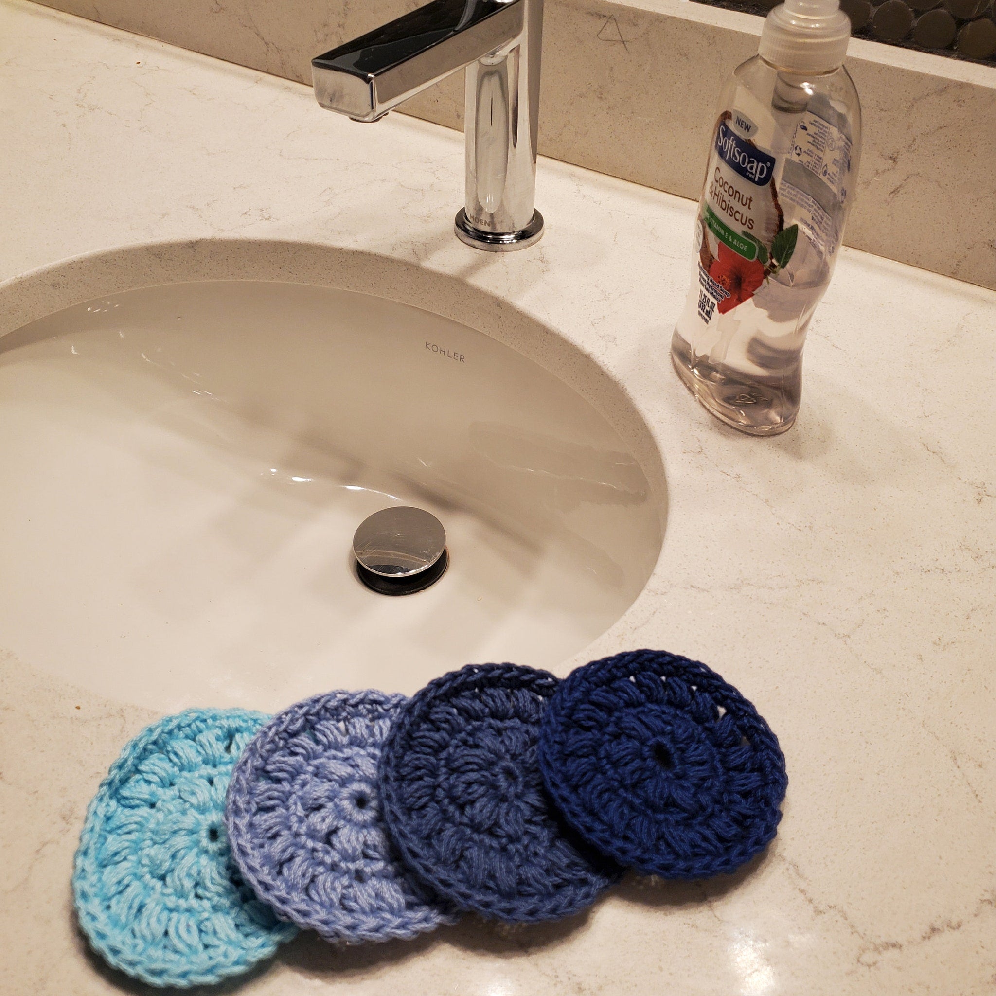 Crochet washcloths in blue hues, circular pattern, placed on bathroom countertop
