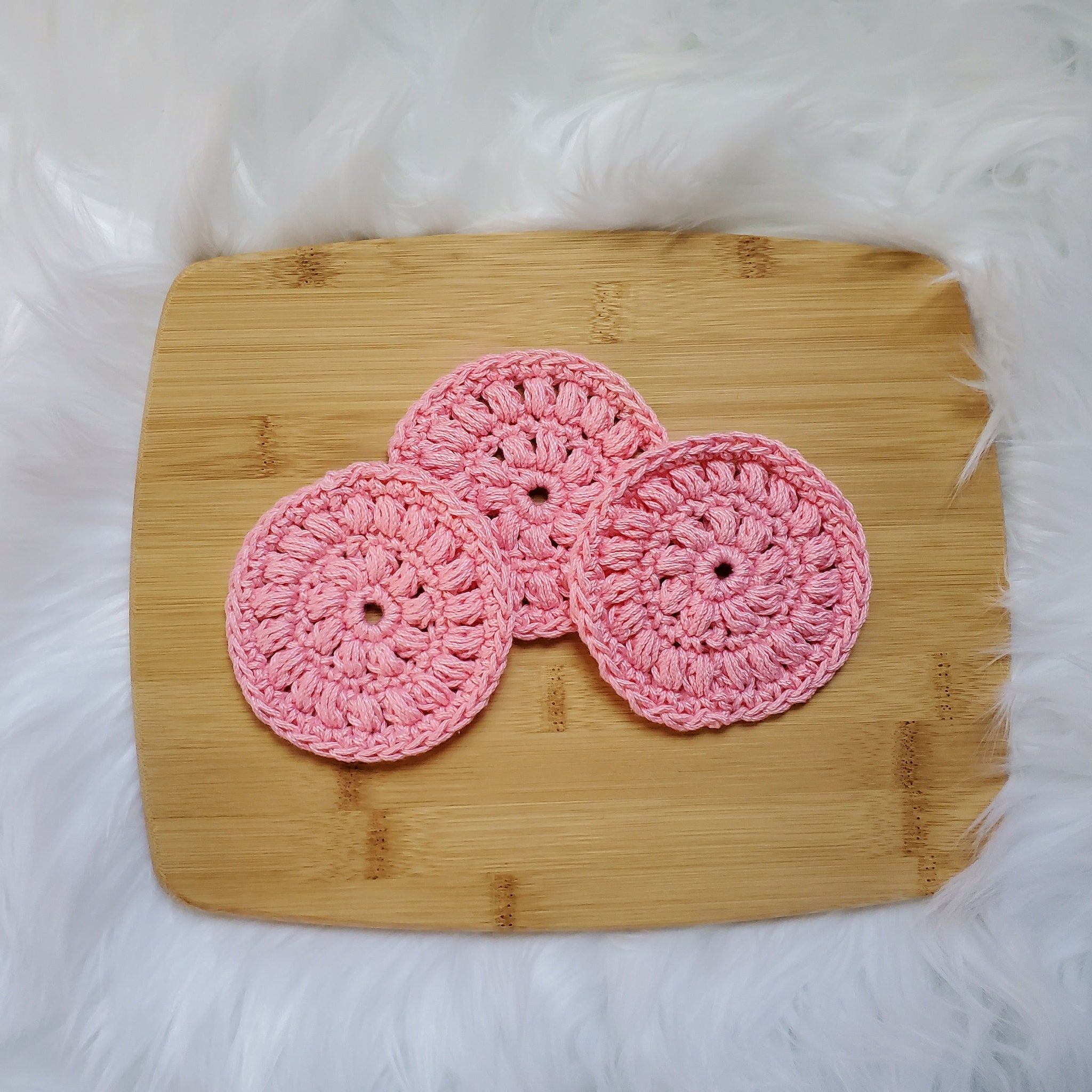 Pink crochet coasters, circular pattern, on wooden cutting board