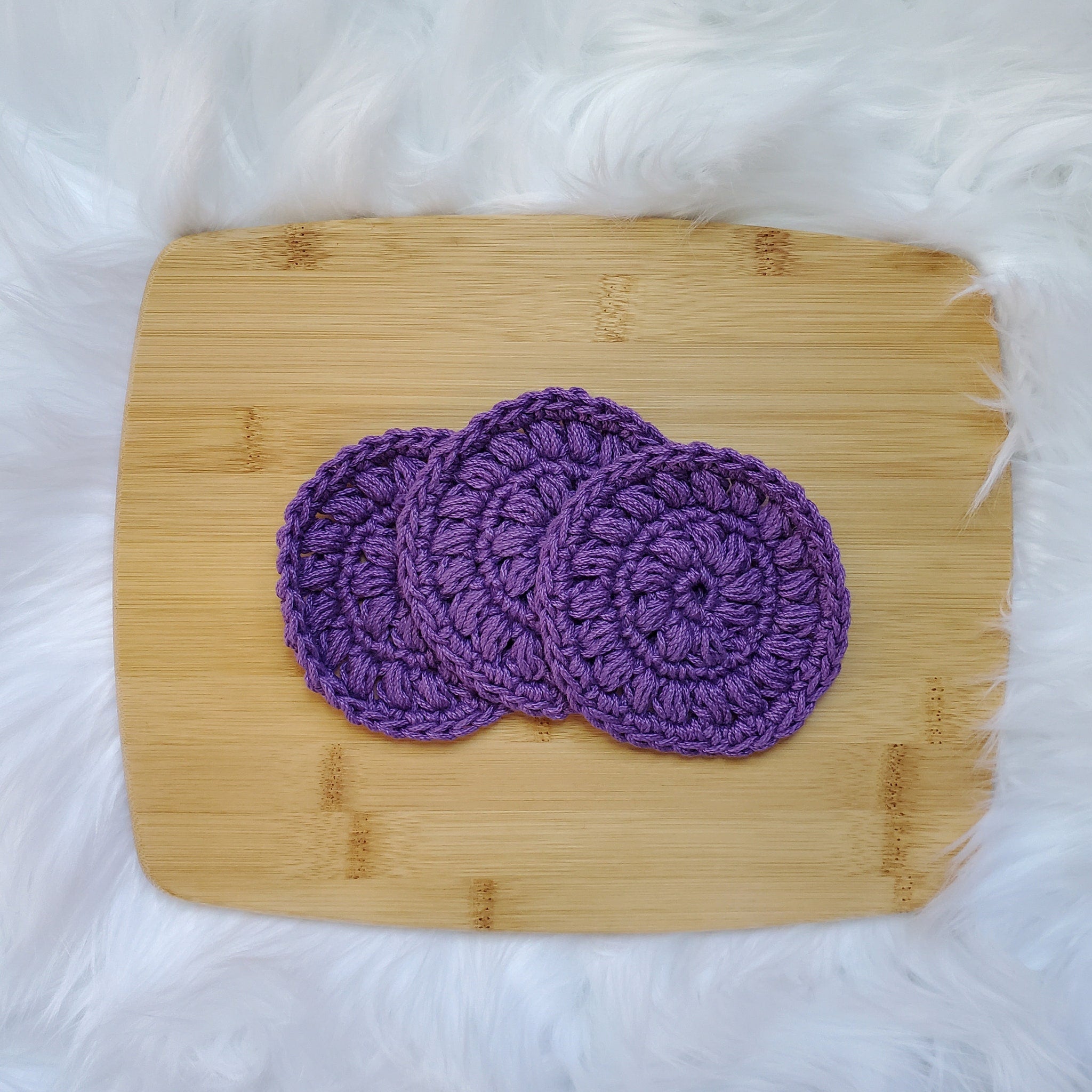Crochet coasters in purple yarn on wooden surface, three circular items