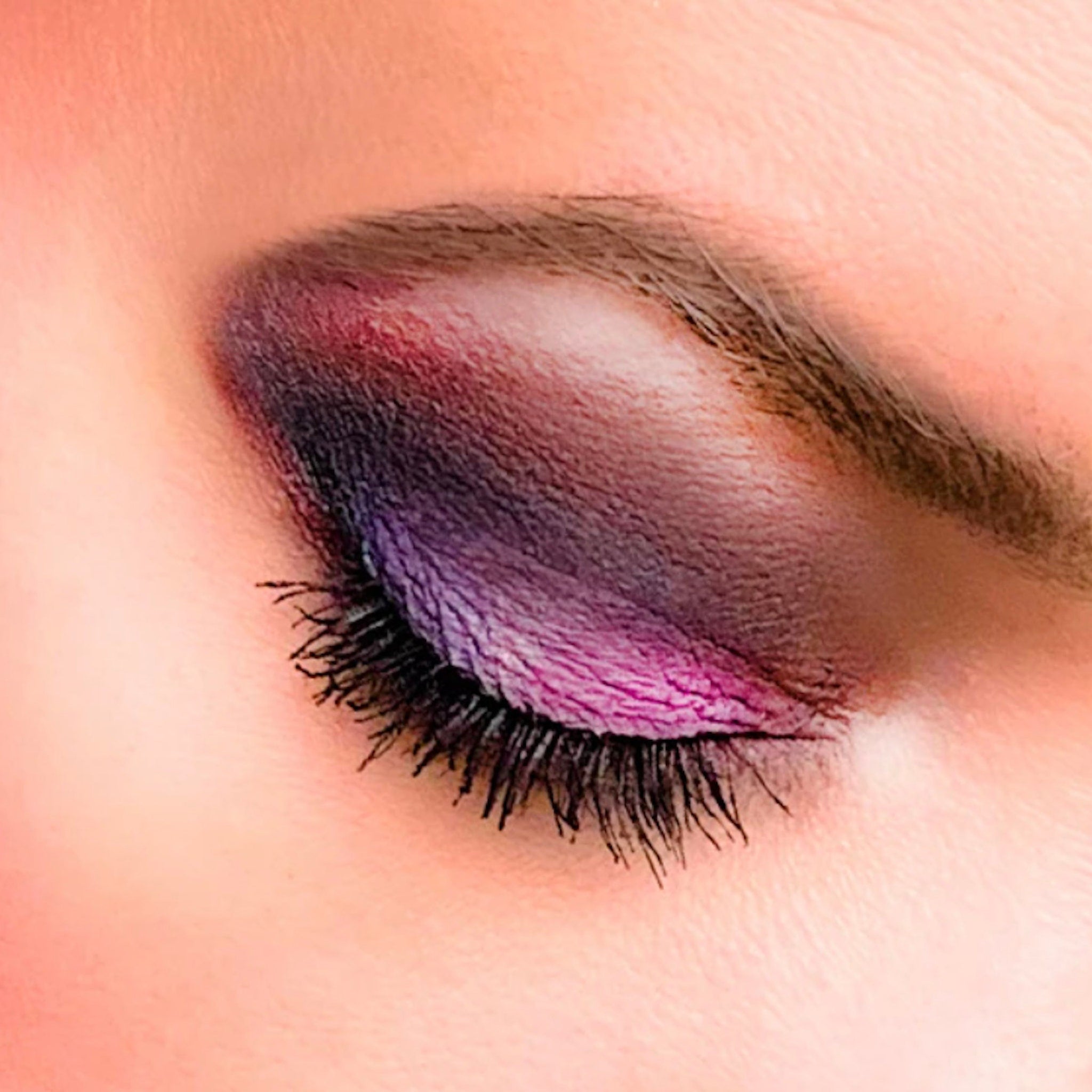 Eye makeup with purple, pink and black shades, applied on closed eye with visible eyelashes