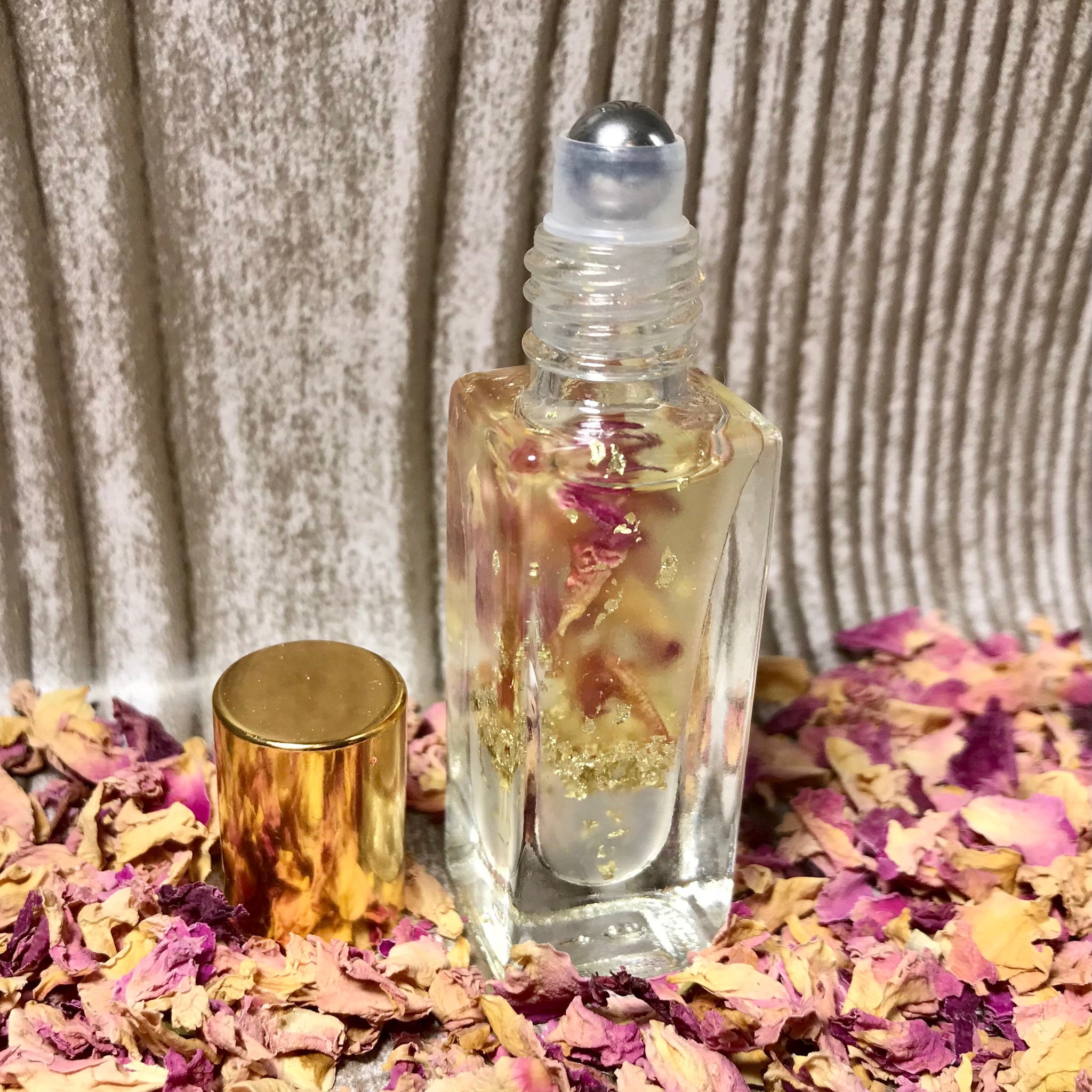 Roll-on perfume bottle with clear glass, gold cap, and floral petals surrounding it