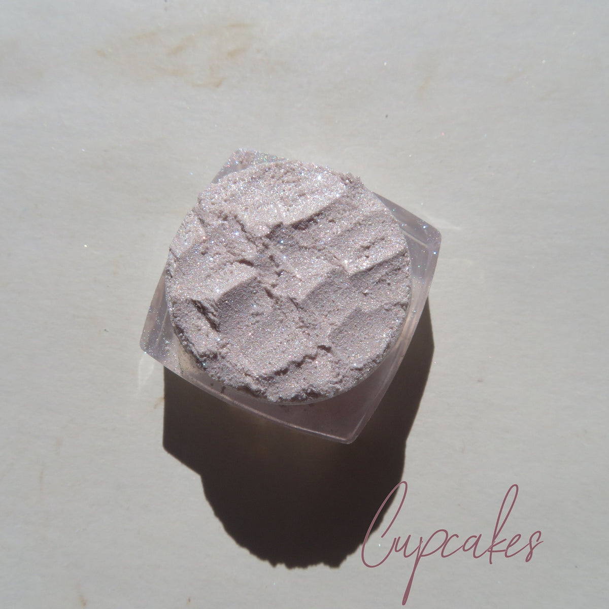 Close-up of sheer pink sparkly glitter eye shadow with shimmer in compact case