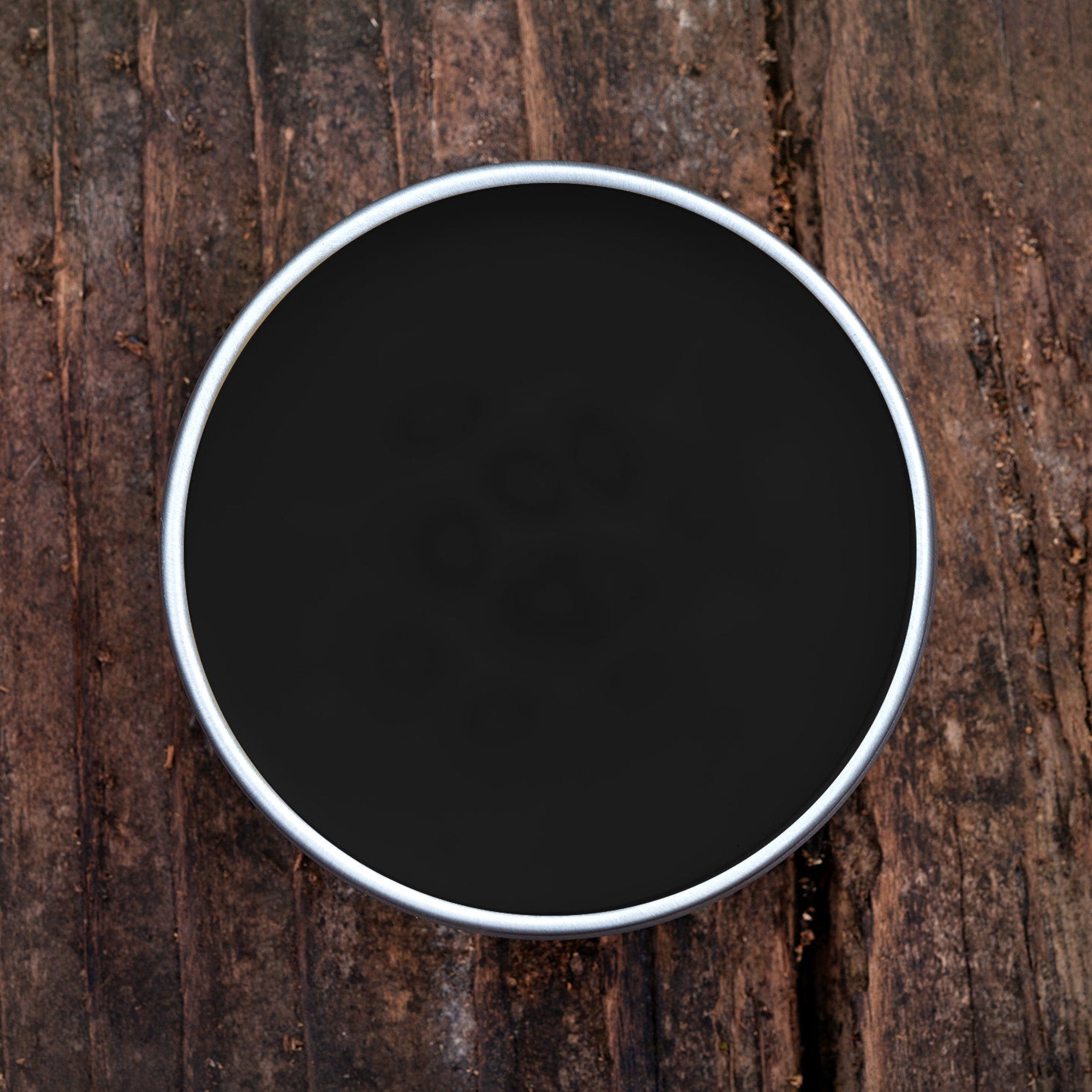 Black round container with silver rim on textured wooden surface