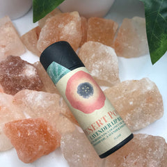 Lip balm tube with Desert Poppy label, black cap, and pink floral design on a bed of orange crystals