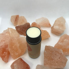 Lip balm tube with beige and black casing, surrounded by orange-pink stones, "Poppy's Balm" text visible