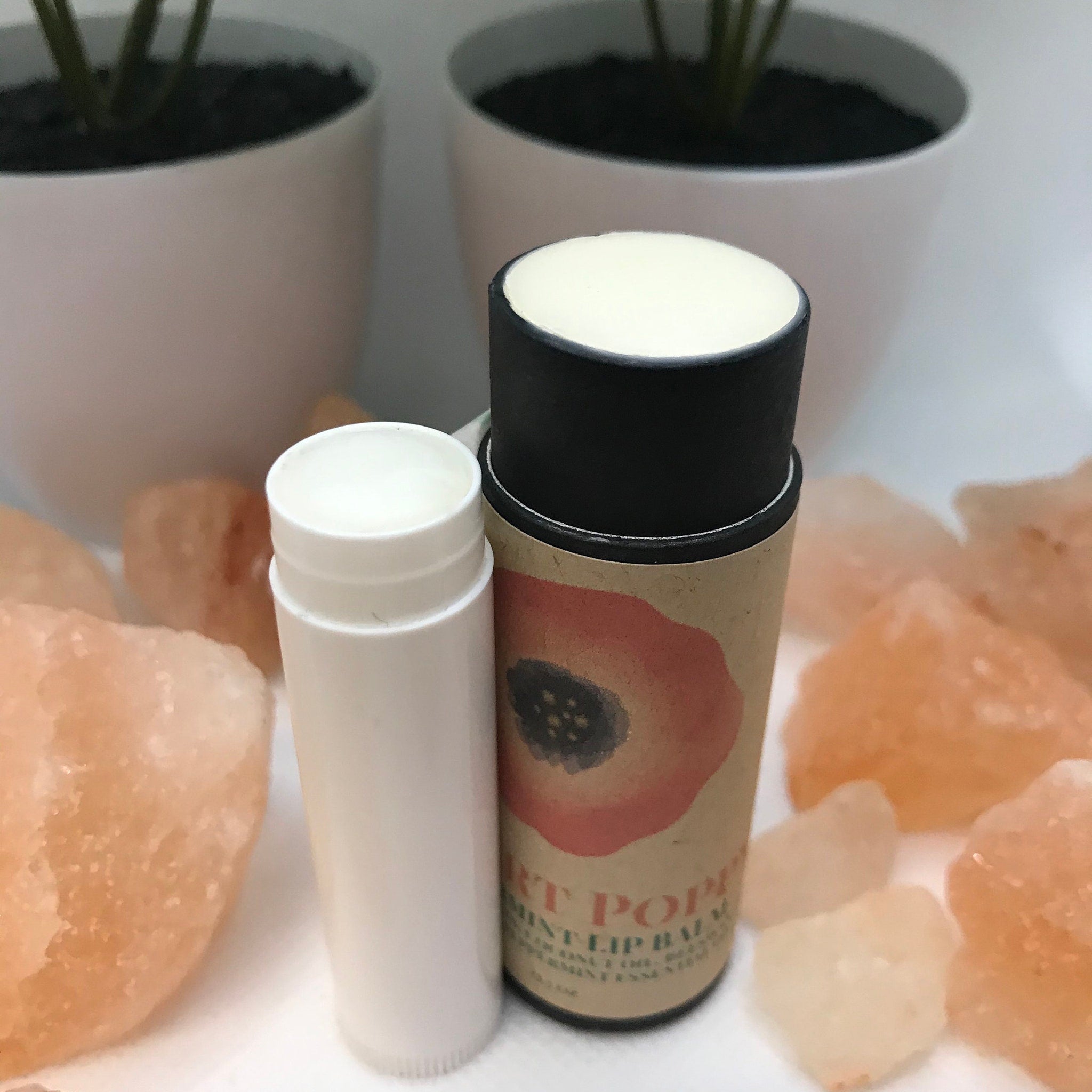 Lip balm tubes with white and black tops, poppy design, and text on a light background