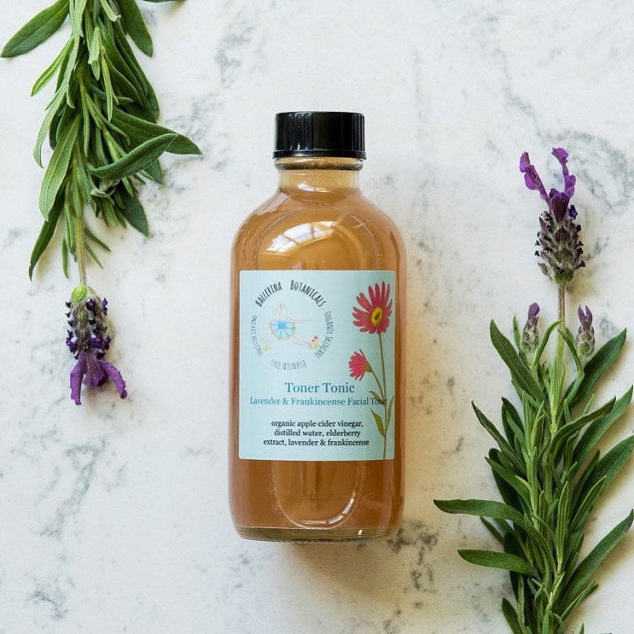 Facial toner bottle with black cap, brown liquid, and brand label, surrounded by lavender and greenery
