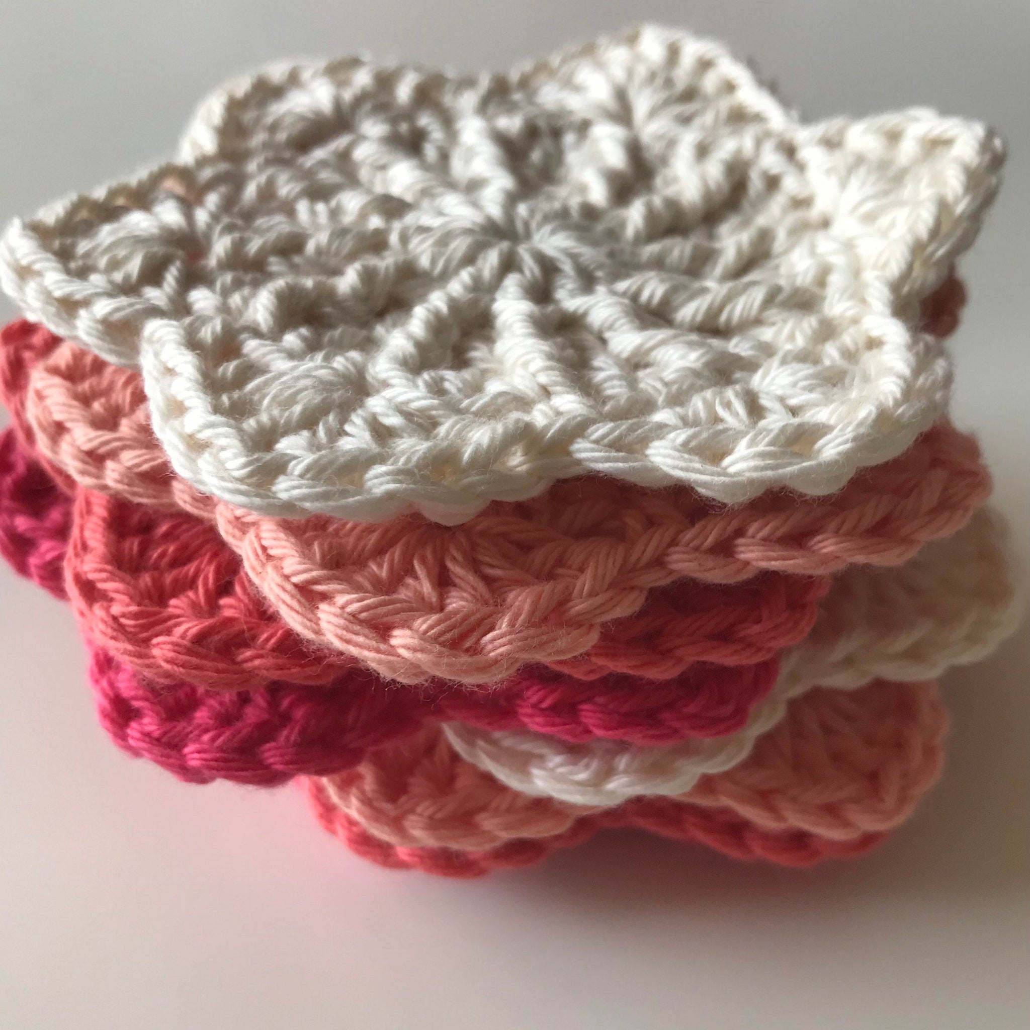 Crochet coasters in white, pink, and peach colors, stacked with a floral design