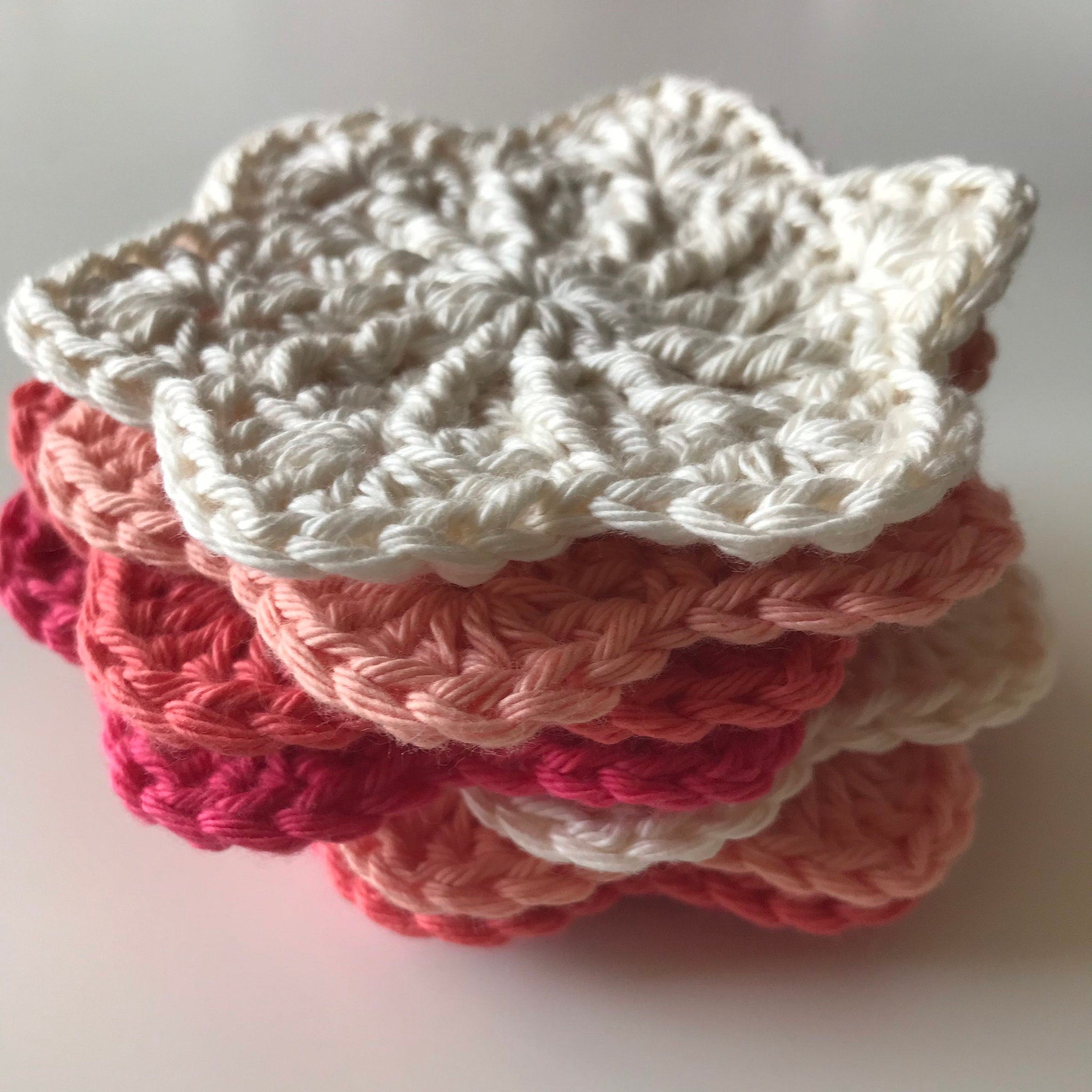 Crochet coasters in white, pink, and coral colors, stacked with a floral design
