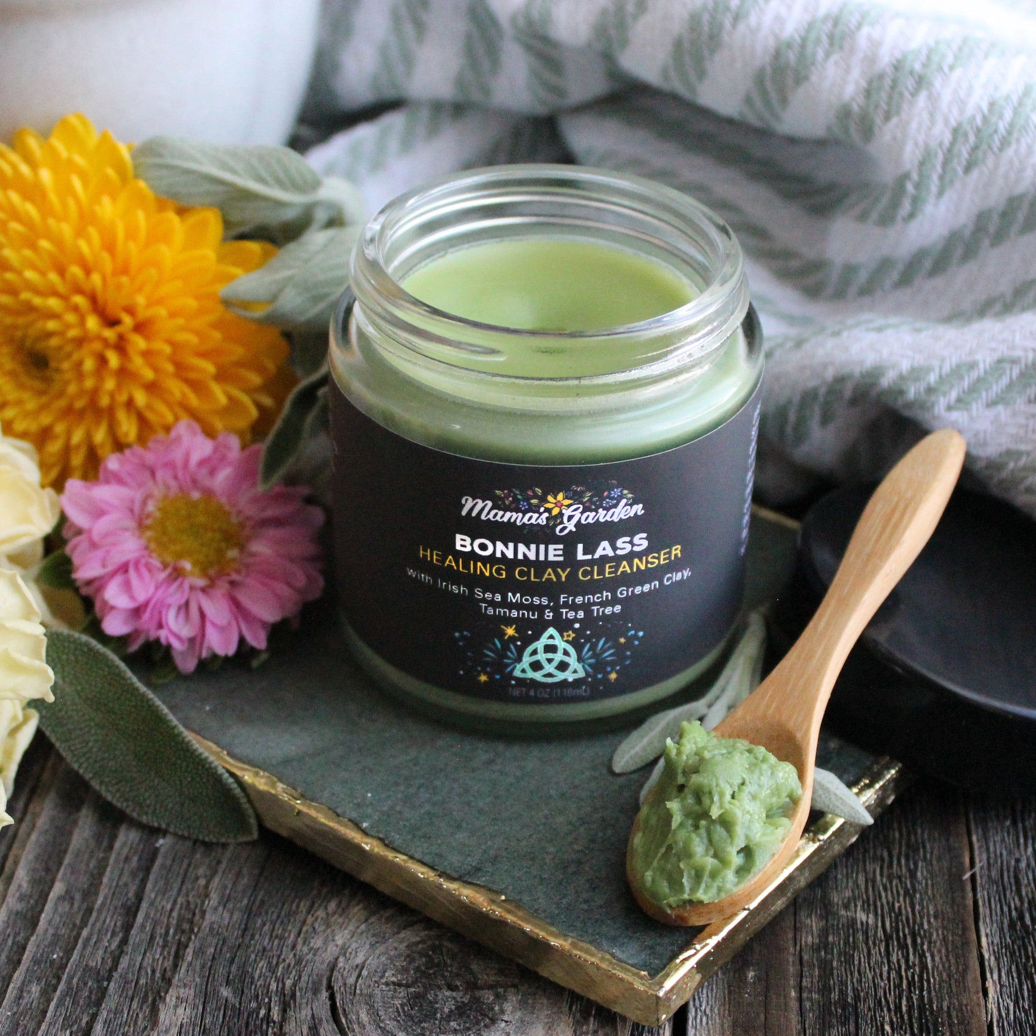 Facial cleanser jar with green contents, wooden spoon, and Mama's Garden label on dark surface